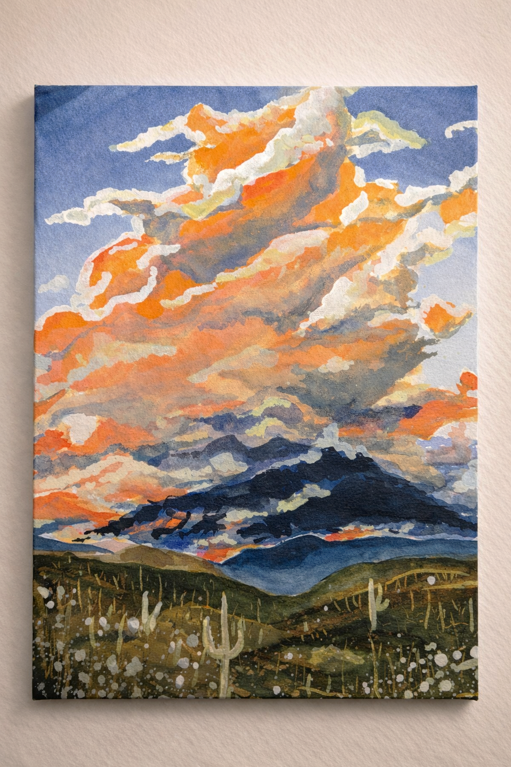 Watercolor painting of a desert landscape with mountains, a sky with orange, yellow, and white clouds, and a few cacti in the foreground.