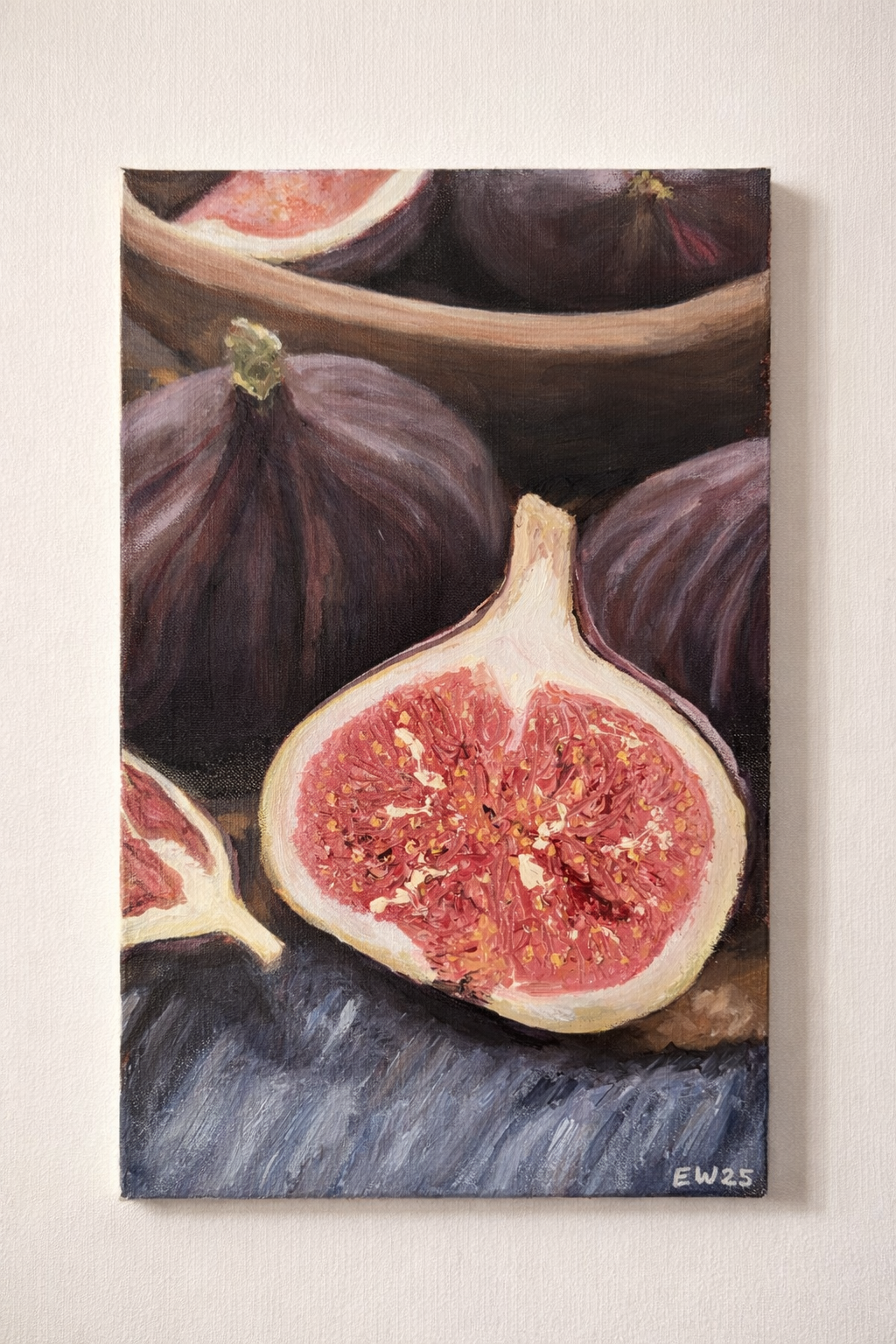 Painting of fresh figs, with one cut open to show its pink interior, placed on a dark textured surface with some figs in a bowl in the background.