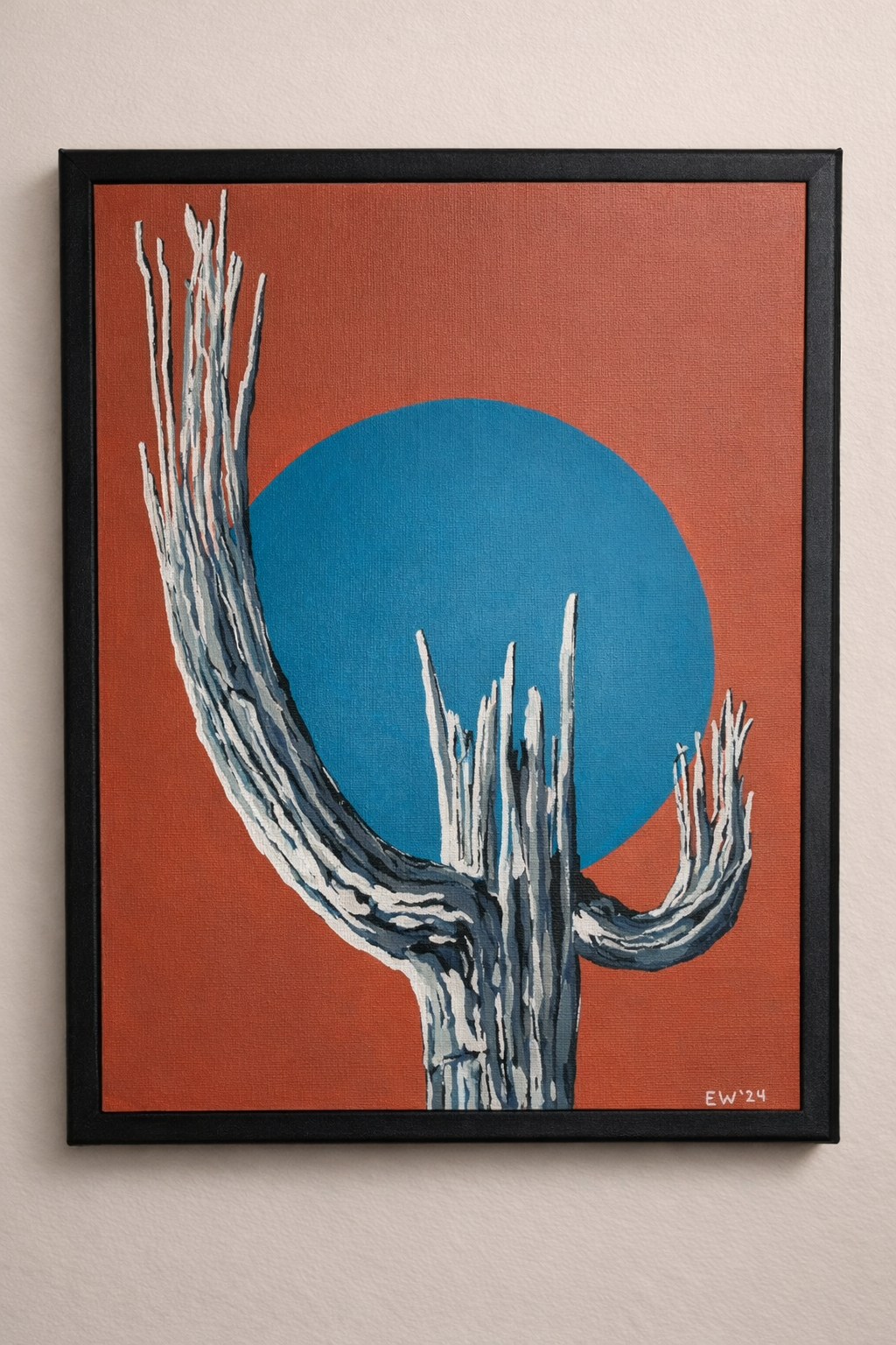 Painted artwork of a white saguaro cactus with a big blue circle in the background on a red-orange wall.