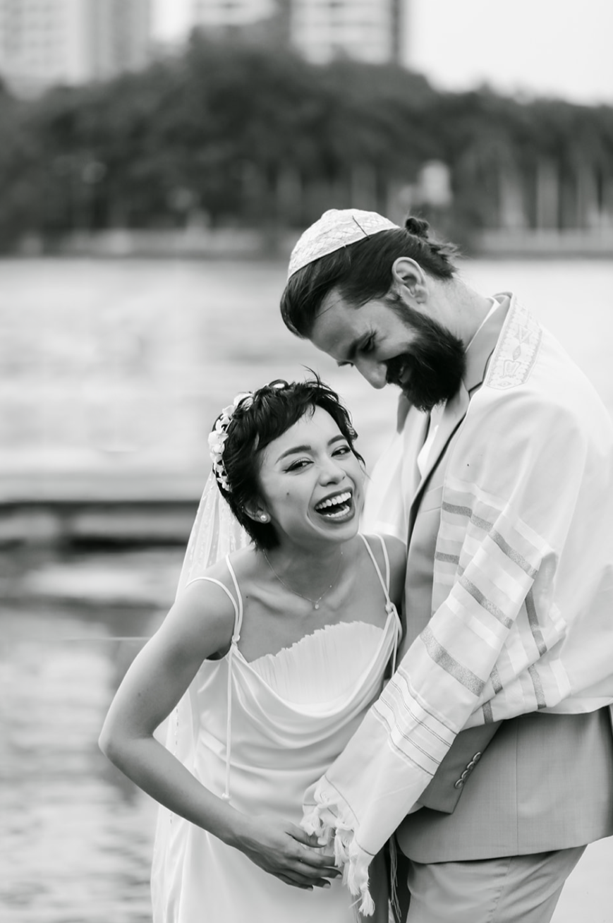 Candid black and white portrait of laughing Vietnamese and Jewish couple during destination wedding in Ho Chi Minh City Vietnam, multicultural and inclusive destination wedding photography by Leah Flores of Wed n Wild, Portland Oregon