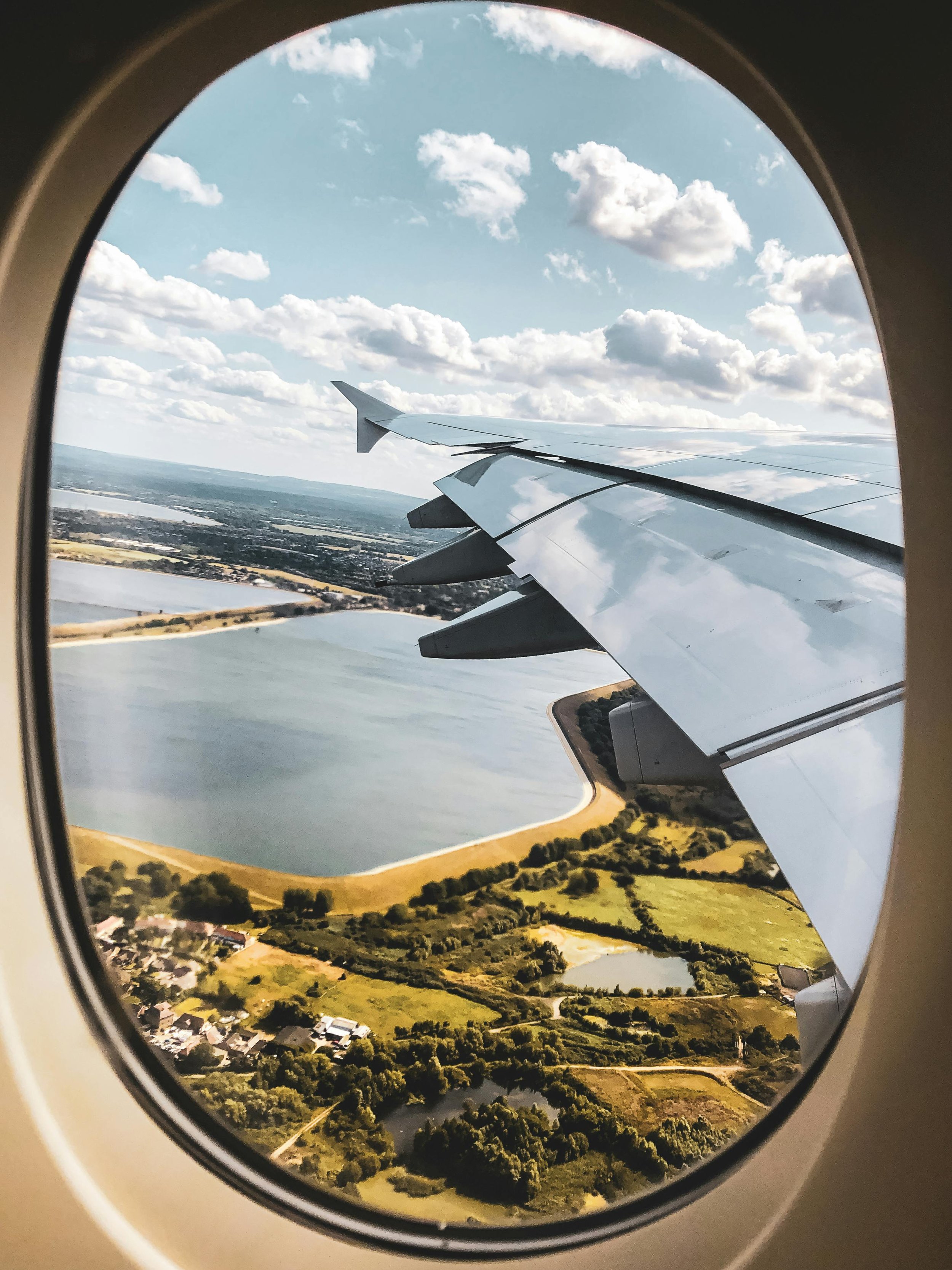 View of a landscape with lakes and greenery seen through an airplane window.