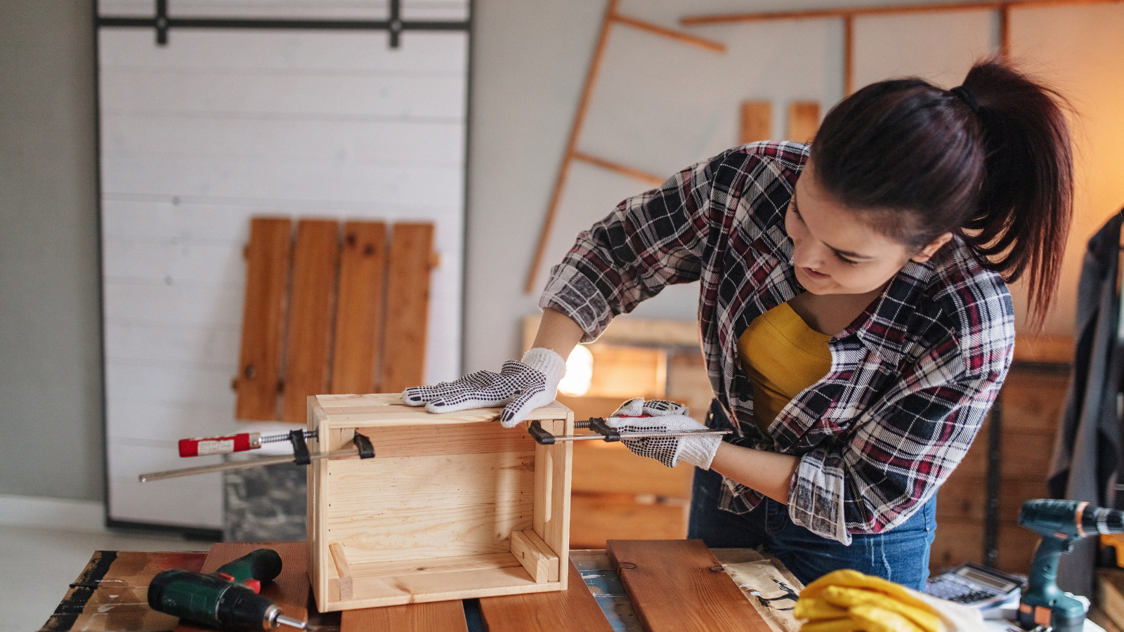 A woman welding a wooden box in a workshop, wearing gloves and focused on her work.