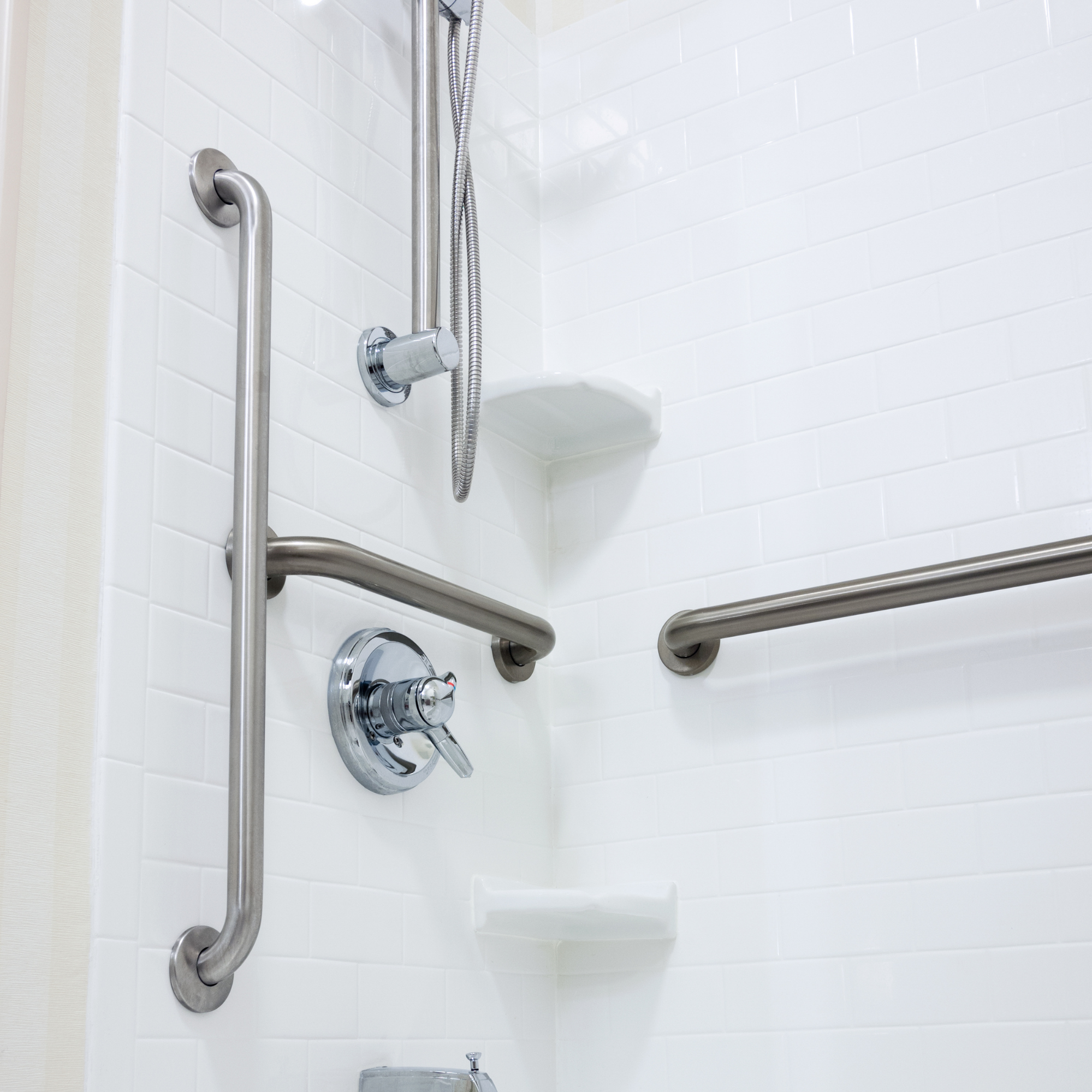 Close-up of a wheelchair accessible shower with grab bars and a handheld shower head.
