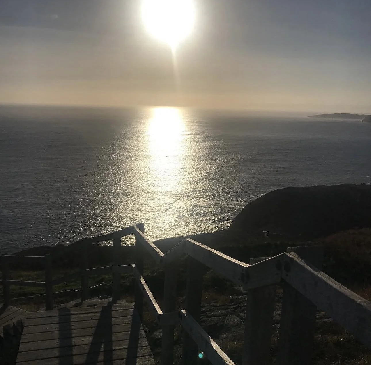 Sunset over the ocean viewed from a coastal wooden staircase with shadows cast on the steps.