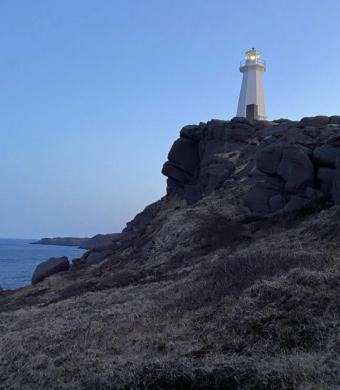 A lighthouse on a rocky cliff overlooking the ocean at dusk.