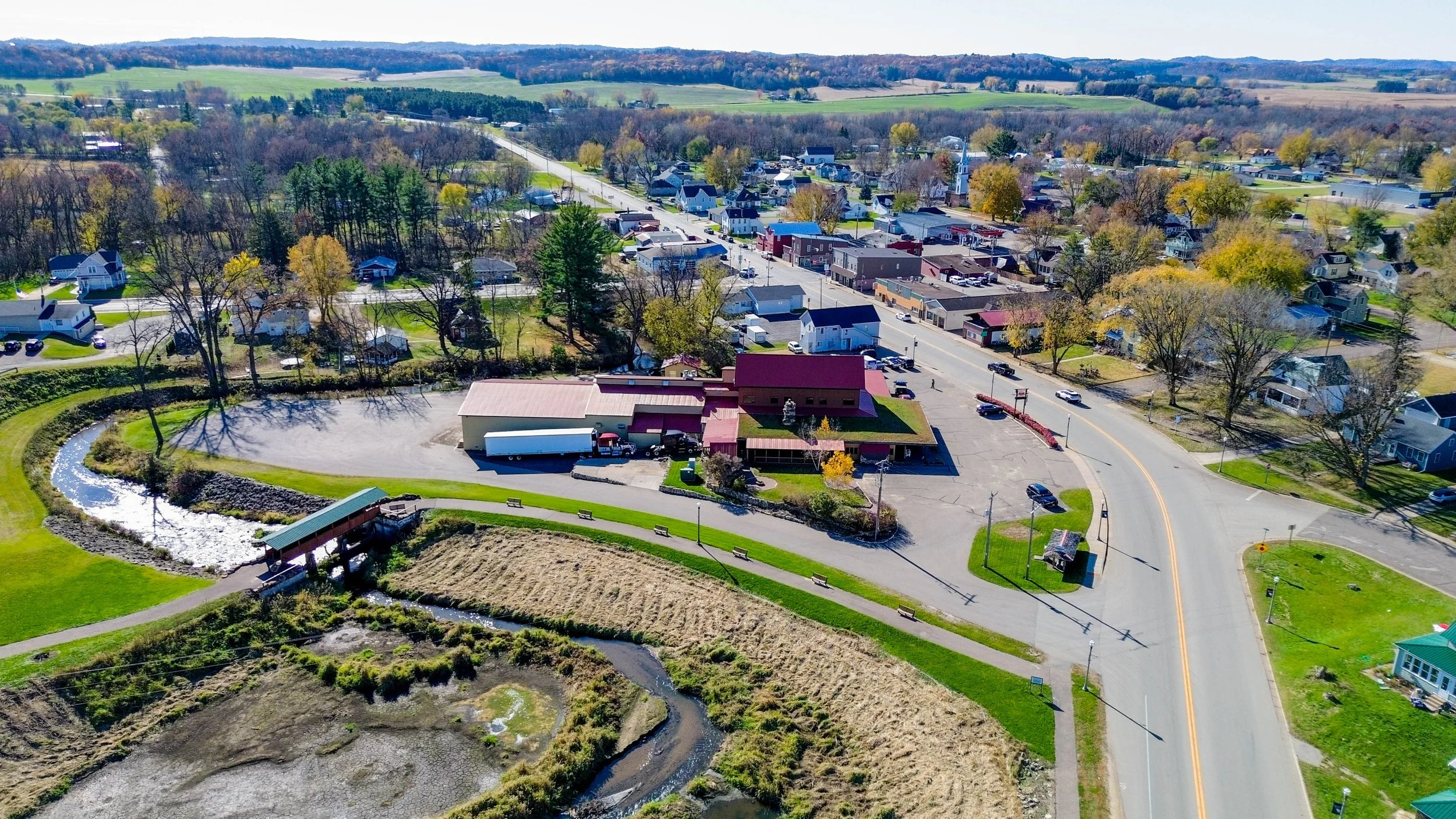 Aerial view of a small town with roads, buildings, houses, trees, a pond, and surrounding farmland.