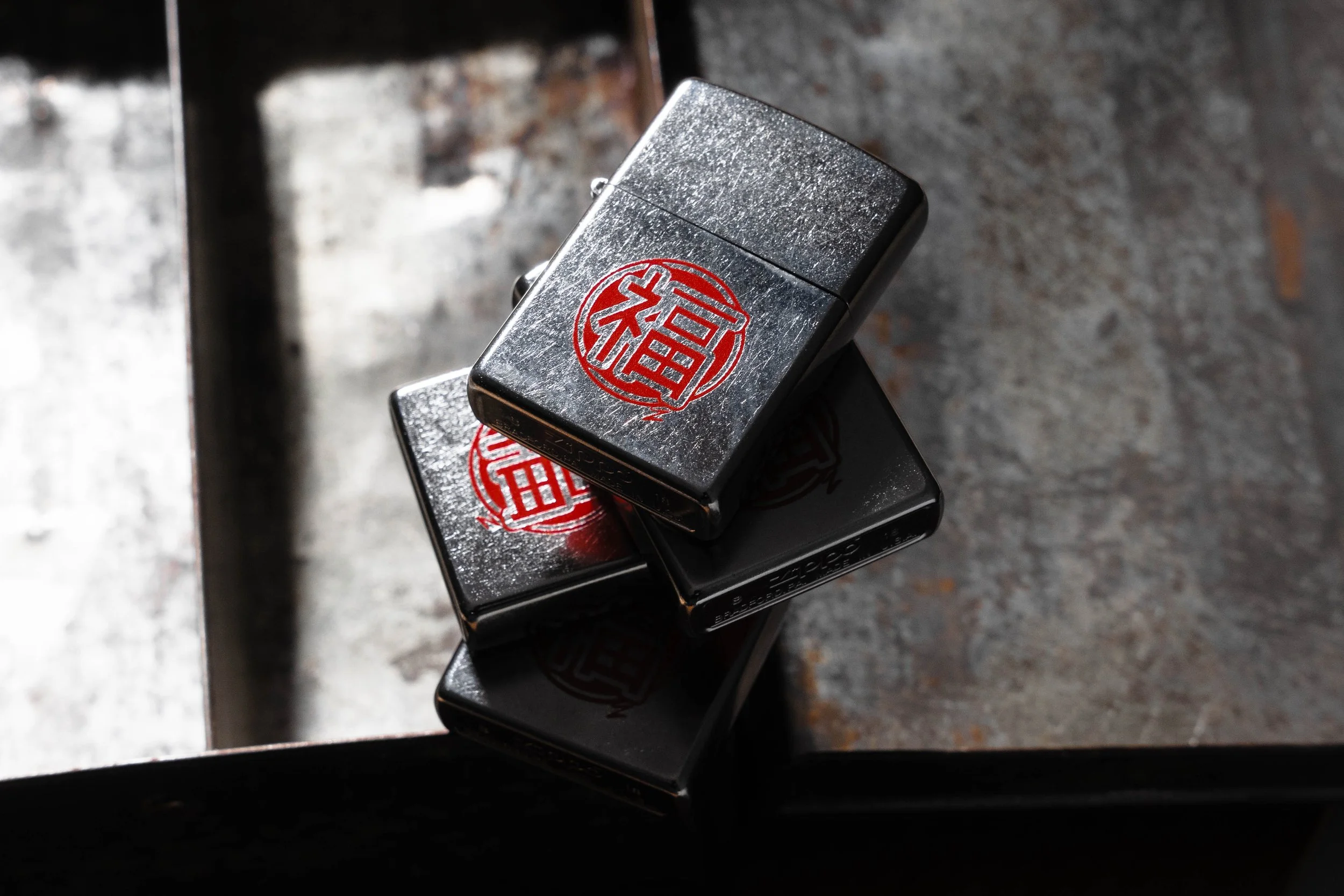 Three stacked dark silver lighters with red Chinese characters on top, placed on a rough concrete surface.