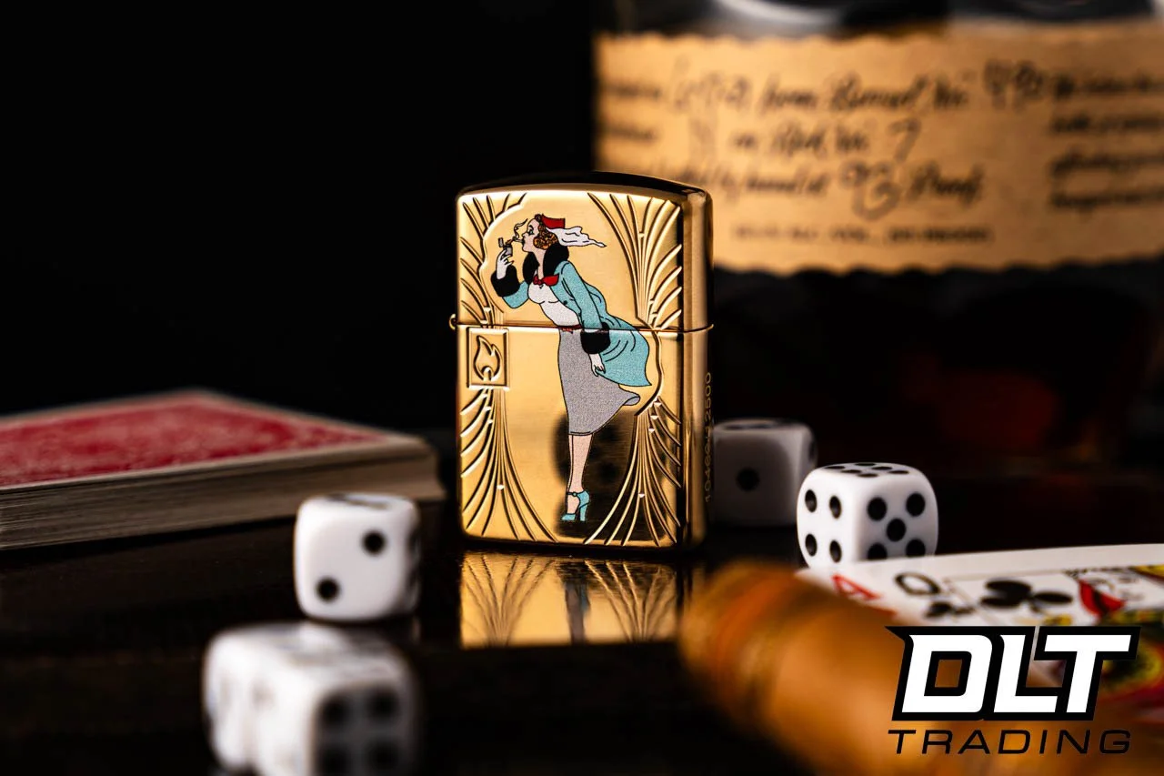 Close-up of a gold-colored lighter with a vintage-style woman illustration, surrounded by scattered dice, a deck of playing cards, and a blurred background with a paper and the DLT Trading logo.