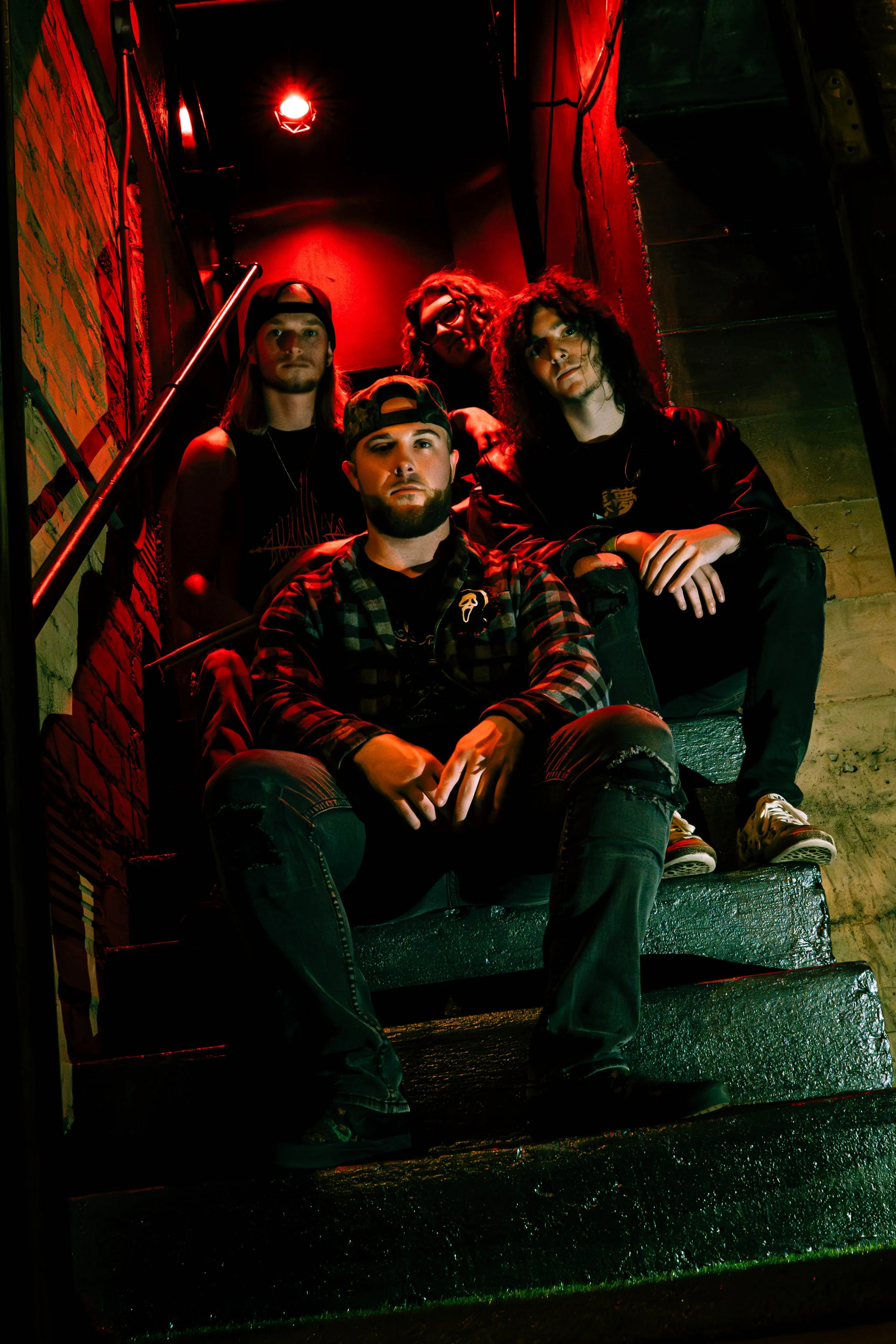 Humanity's Downfall sitting on stairway with dark, moody lighting and red glow, some wearing casual streetwear