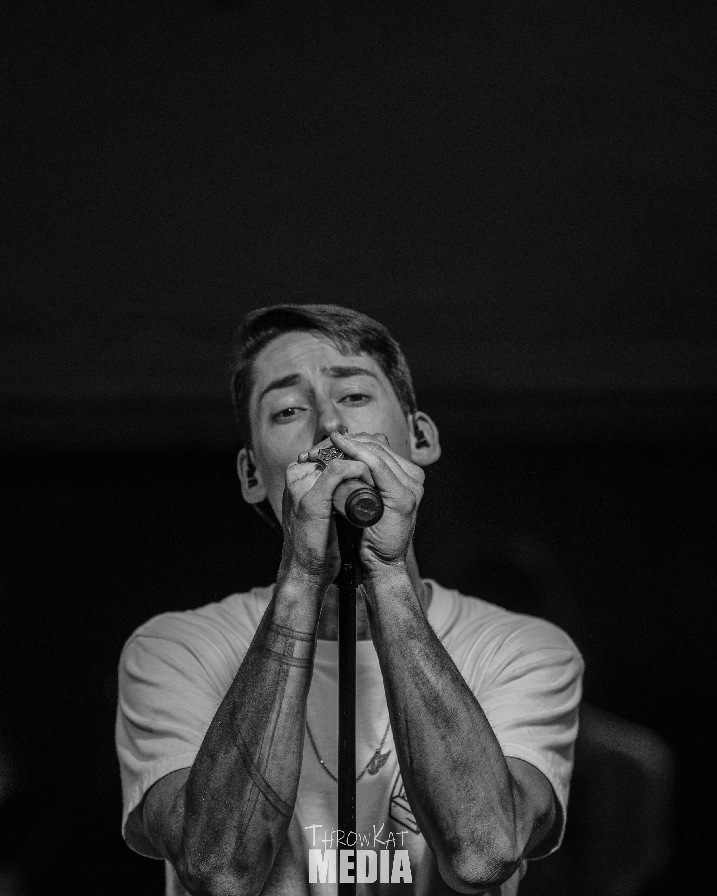 A young man singing into a microphone. Black and white photo, focused on his face and hands.