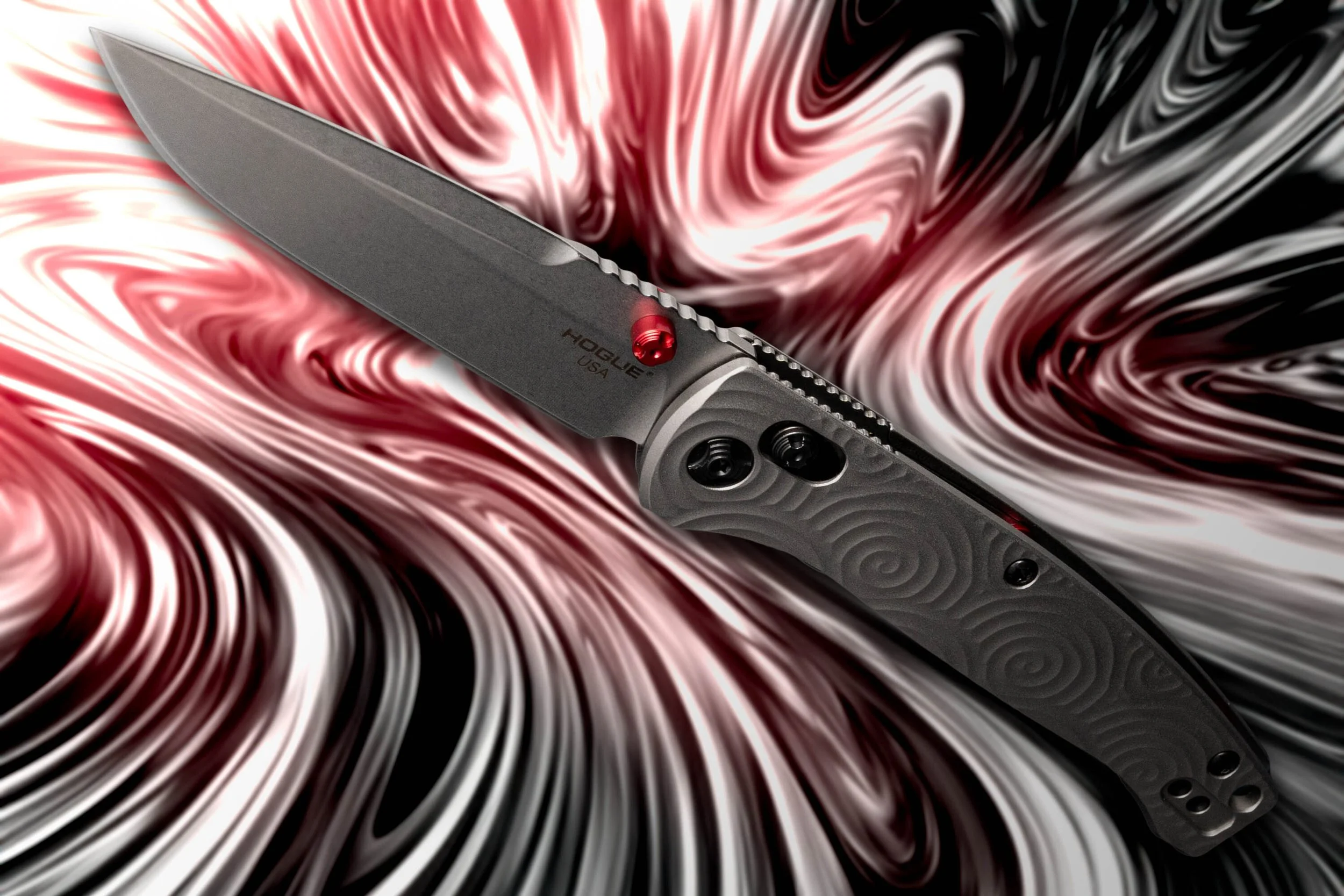 A tactical folding knife with a black blade and textured gray handle, resting on a swirling red, black, and white background.