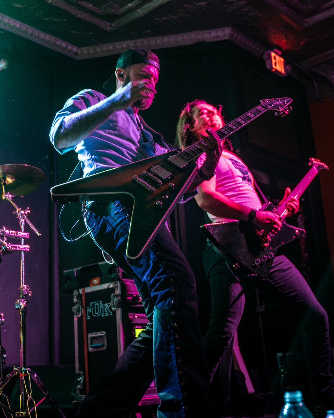 Two musicians playing electric guitars on stage under colorful lighting.
