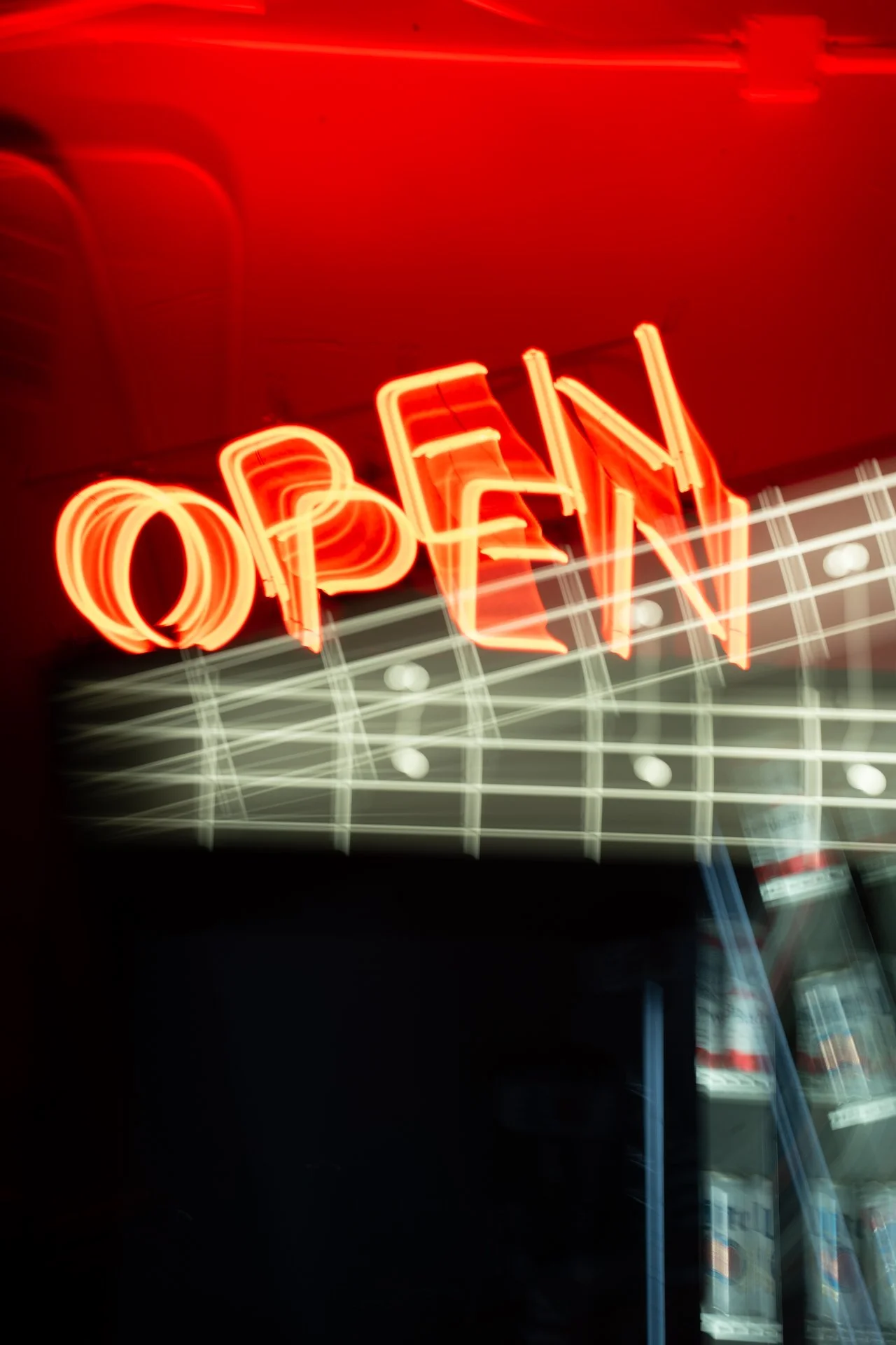 Bright red neon sign spelling out 'OPEN' against a dark background, next to a beverage refrigerator.