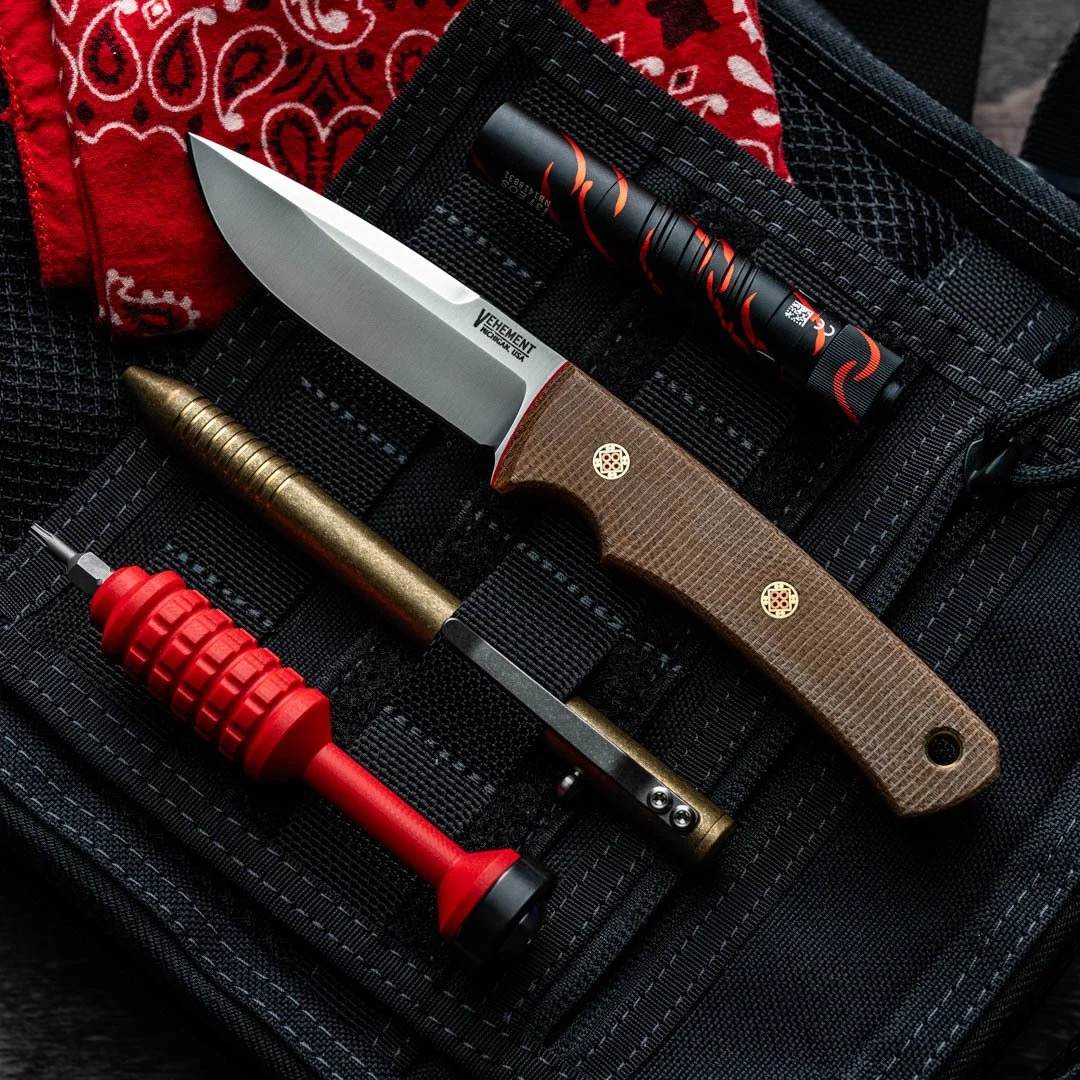 A fixed-blade knife with a wooden handle, a brass pen, a red and black sealing wax tool, and a black flashlight with red accents are arranged on a black tactical pouch with elastic straps.