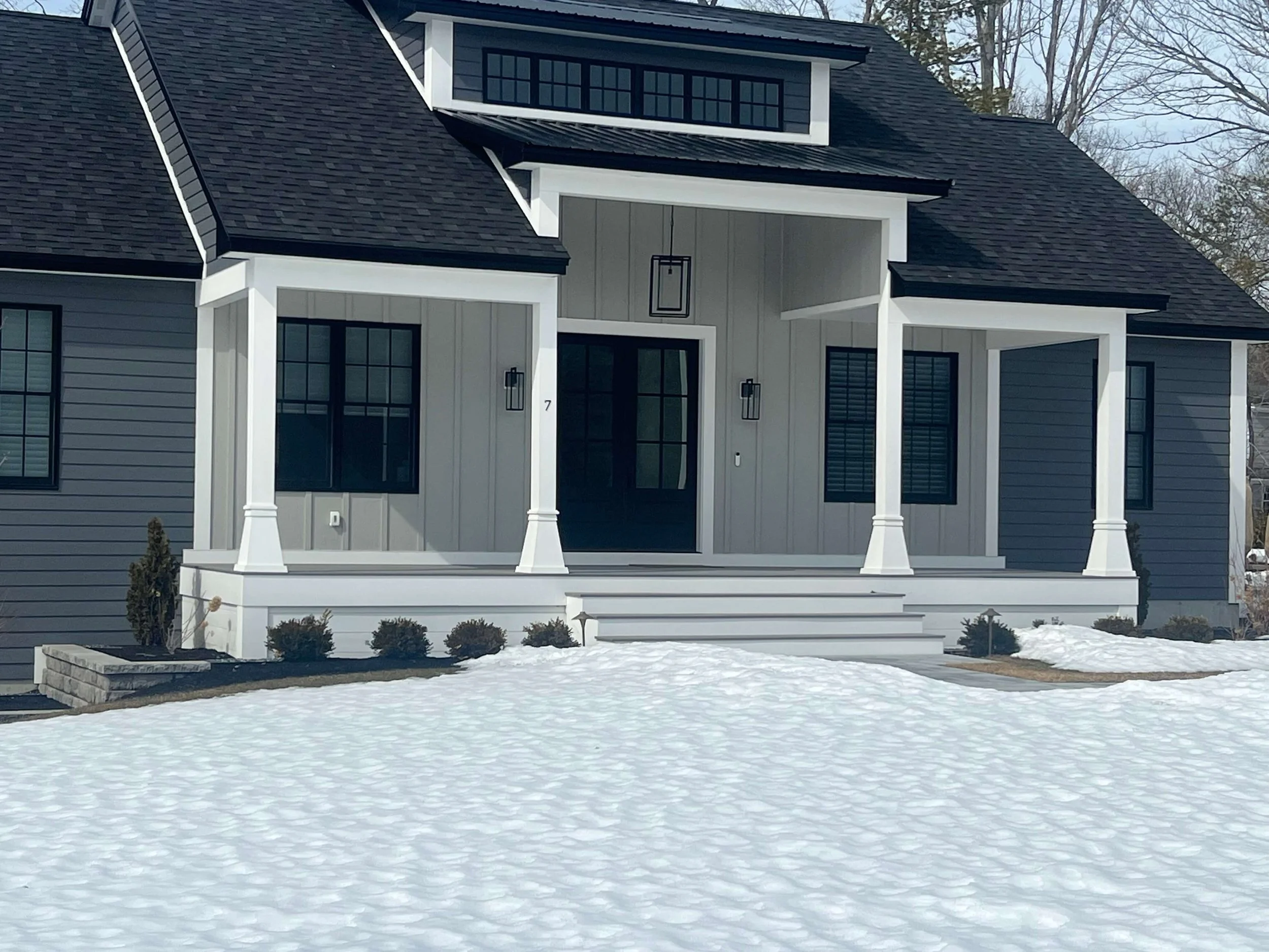 Front view of a modern house with a porch, four steps leading up to the entrance, and snow on the ground.