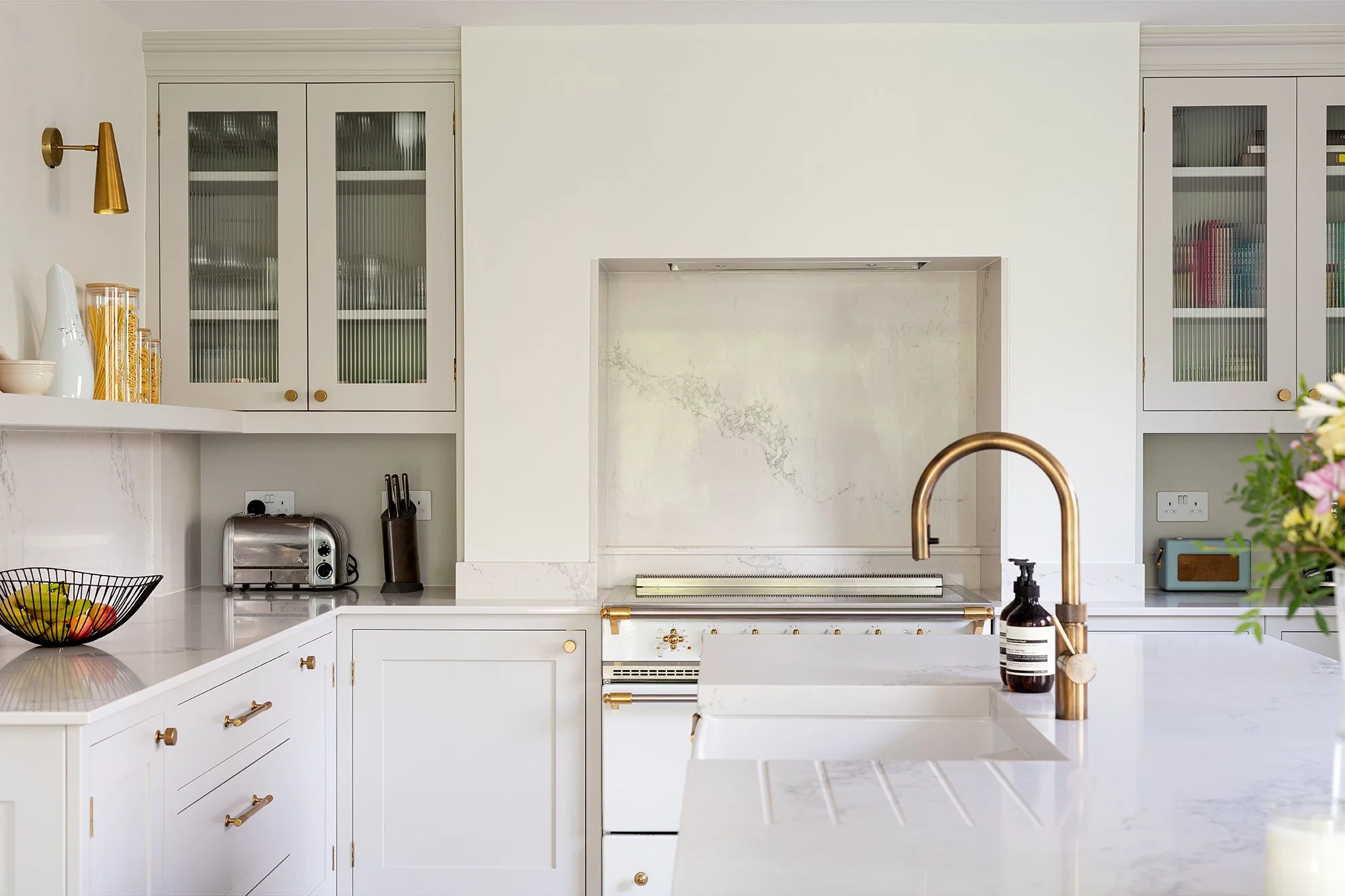 Modern white kitchen with gold accents, marble countertops, and glass-front cabinets.