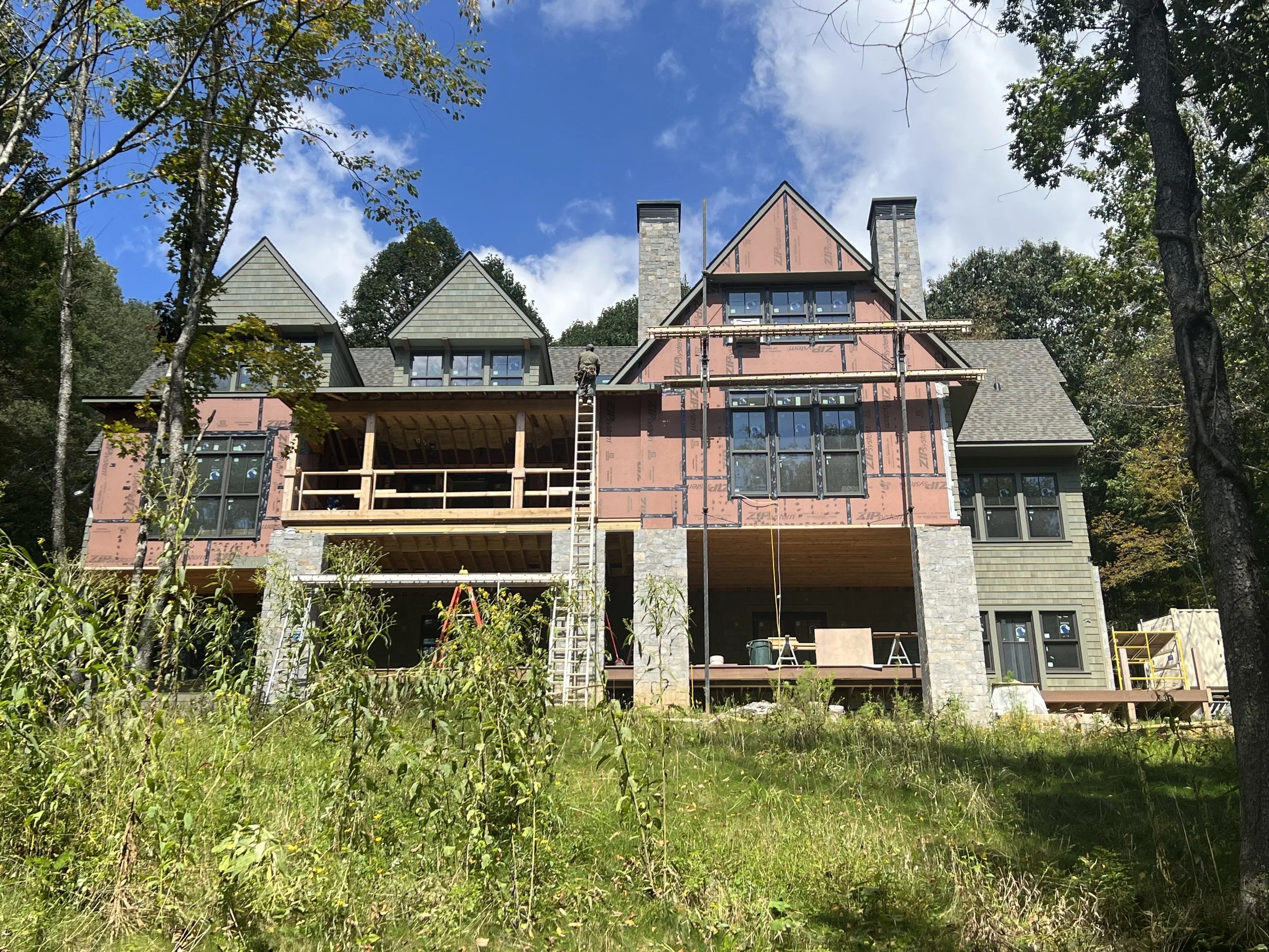House under construction seen through trees with blue sky and clouds in the background.