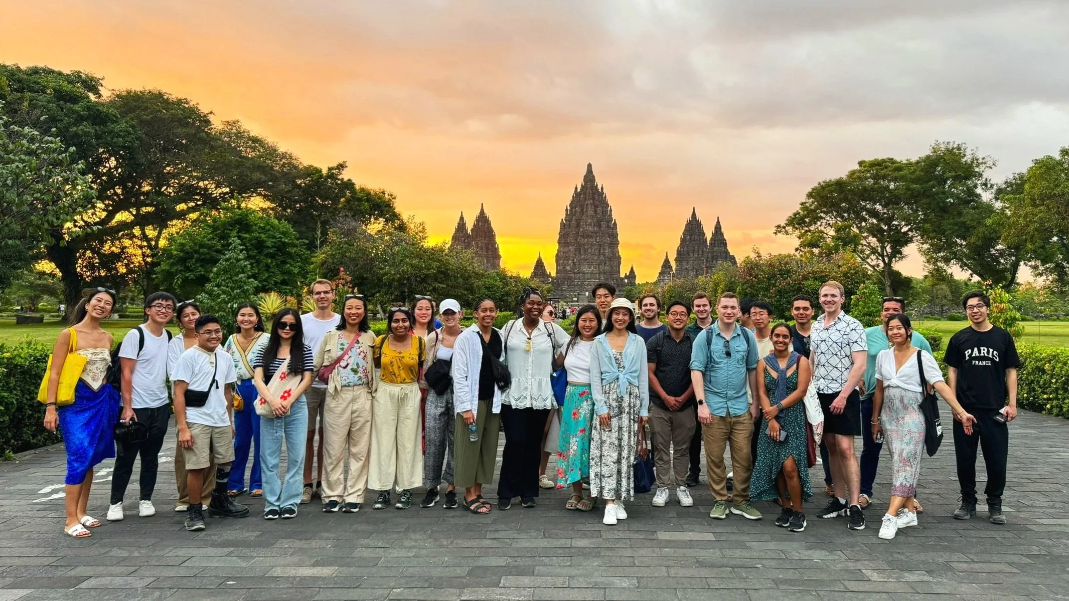 Group of diverse people standing outdoors at sunset, with historic temples and lush greenery in the background.