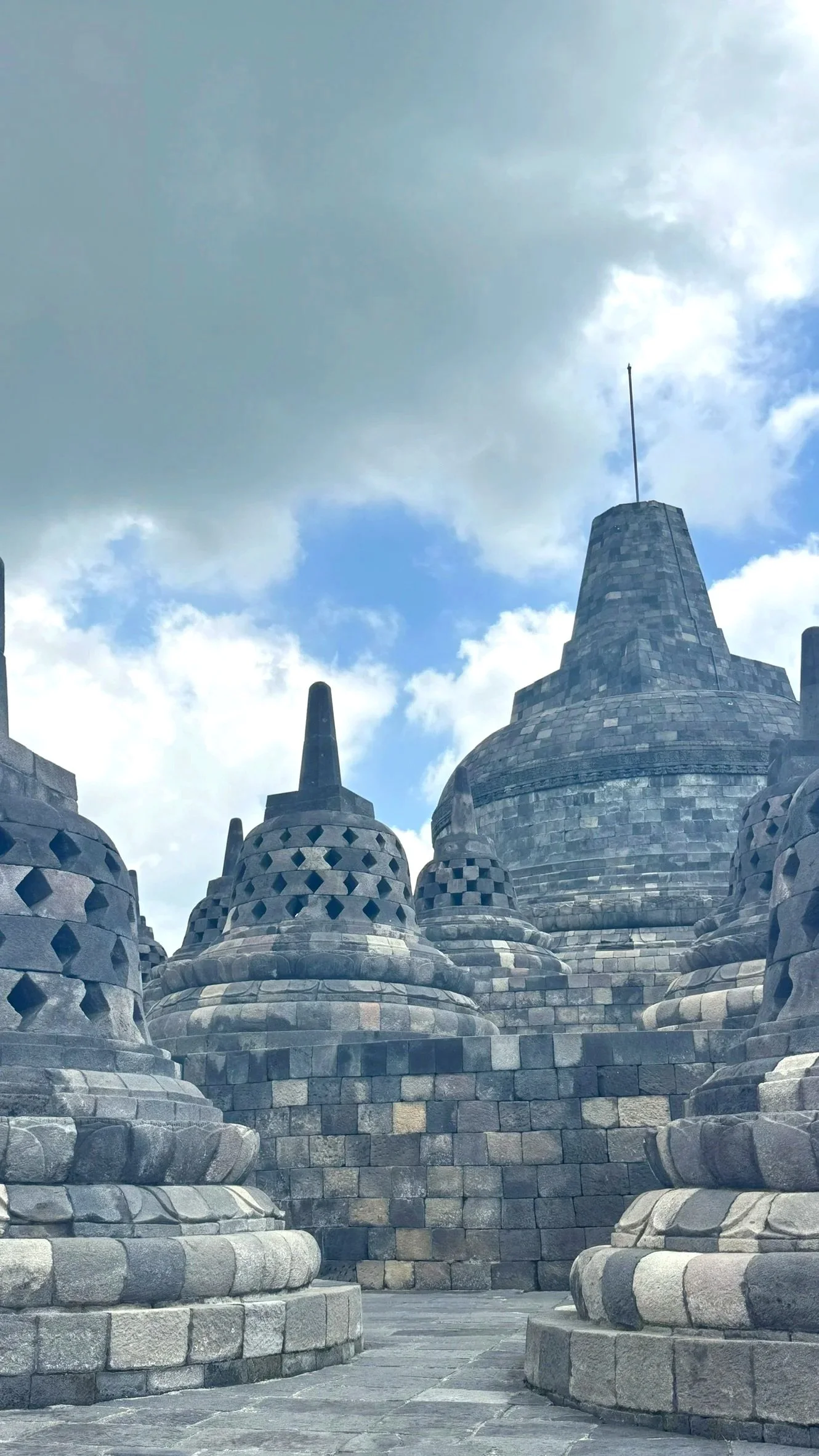 Ancient Buddhist temples in a row with stone pagodas and a large stupa, cloudy sky in the background.