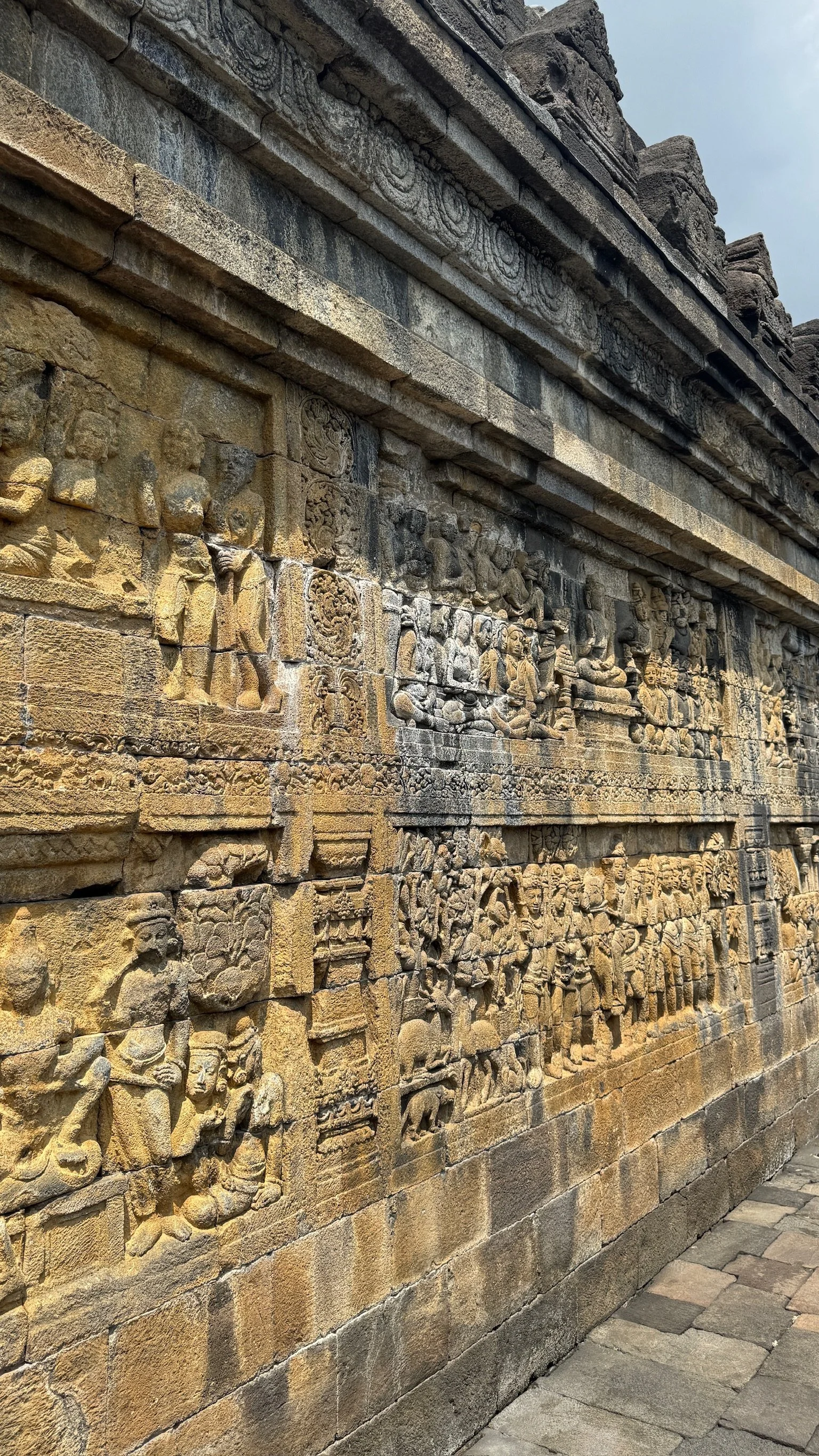 Ancient stone wall with detailed carvings of human figures, animals, and decorative patterns, likely part of a historic temple or monument.