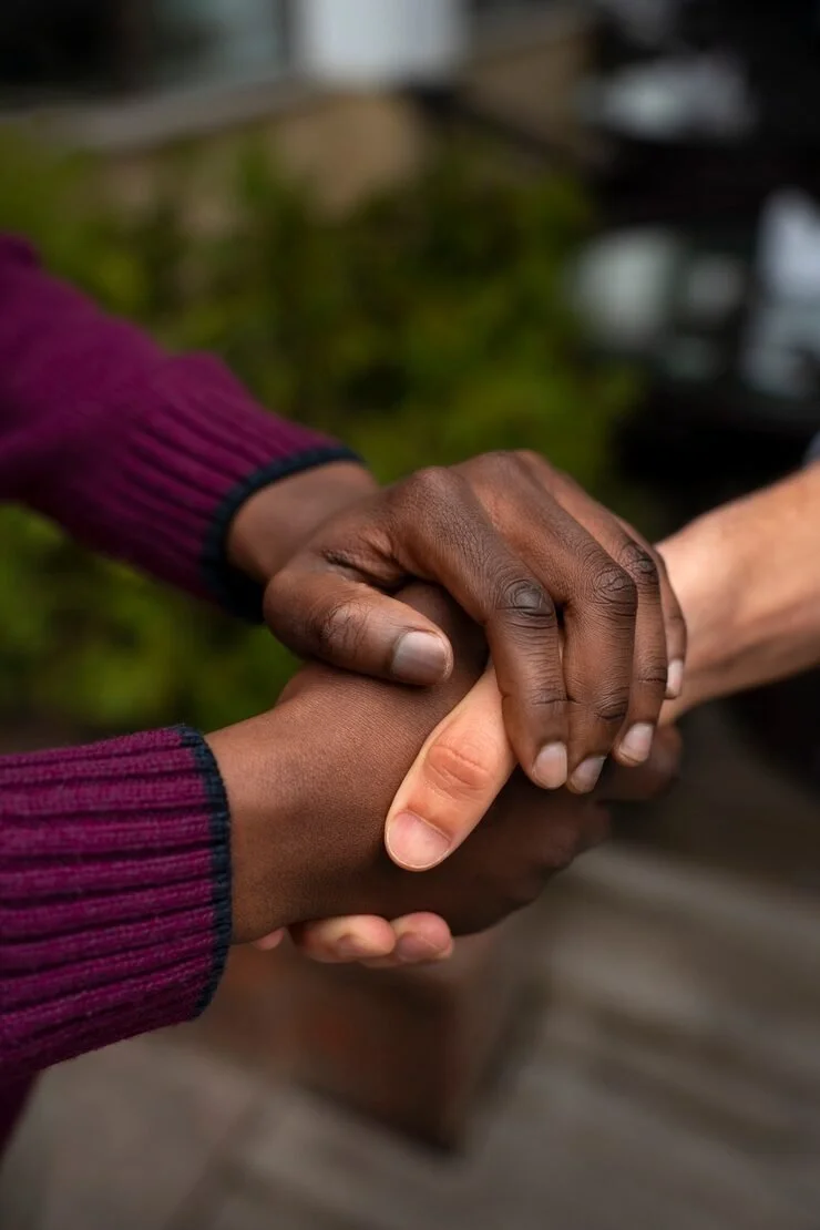 Two people shaking hands outdoors, one with a darker skin tone and the other with a lighter skin tone.