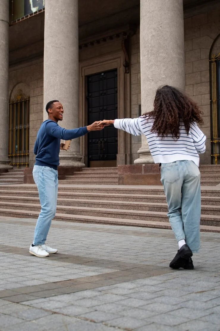 A young man and woman are high-fiving outside a large building with stone columns and stairs.