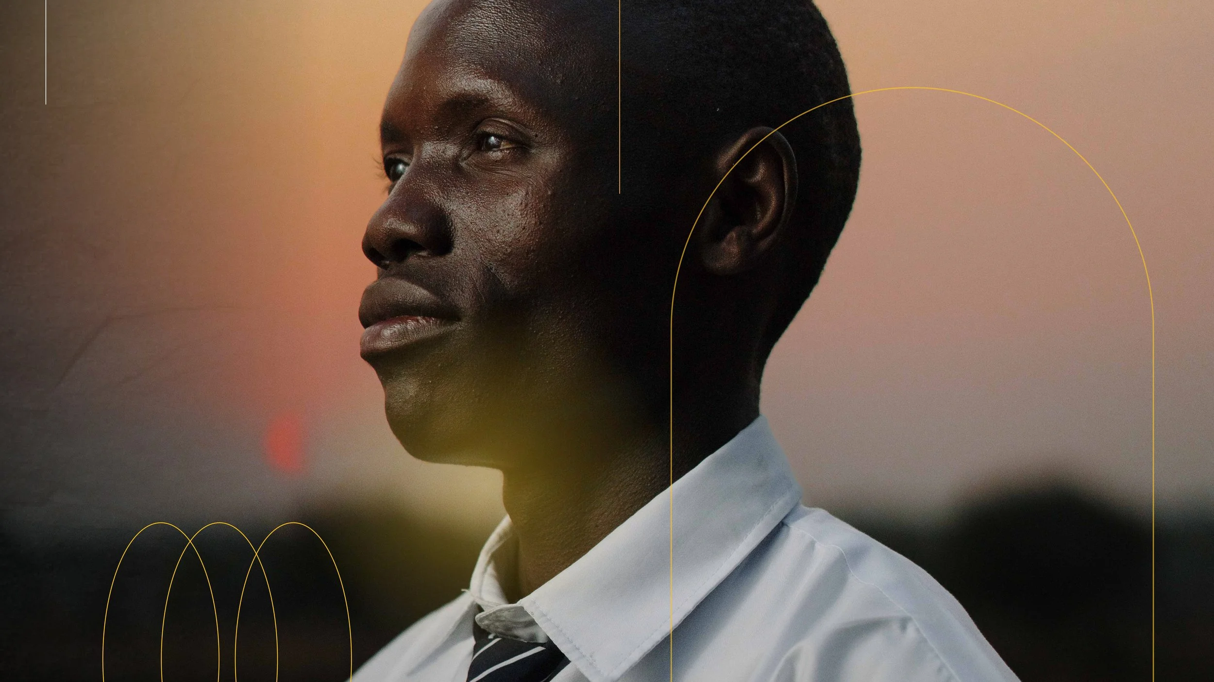 Close-up of a young Black man in a white shirt and dark tie, gazing thoughtfully to the side, with a blurred sunset background.