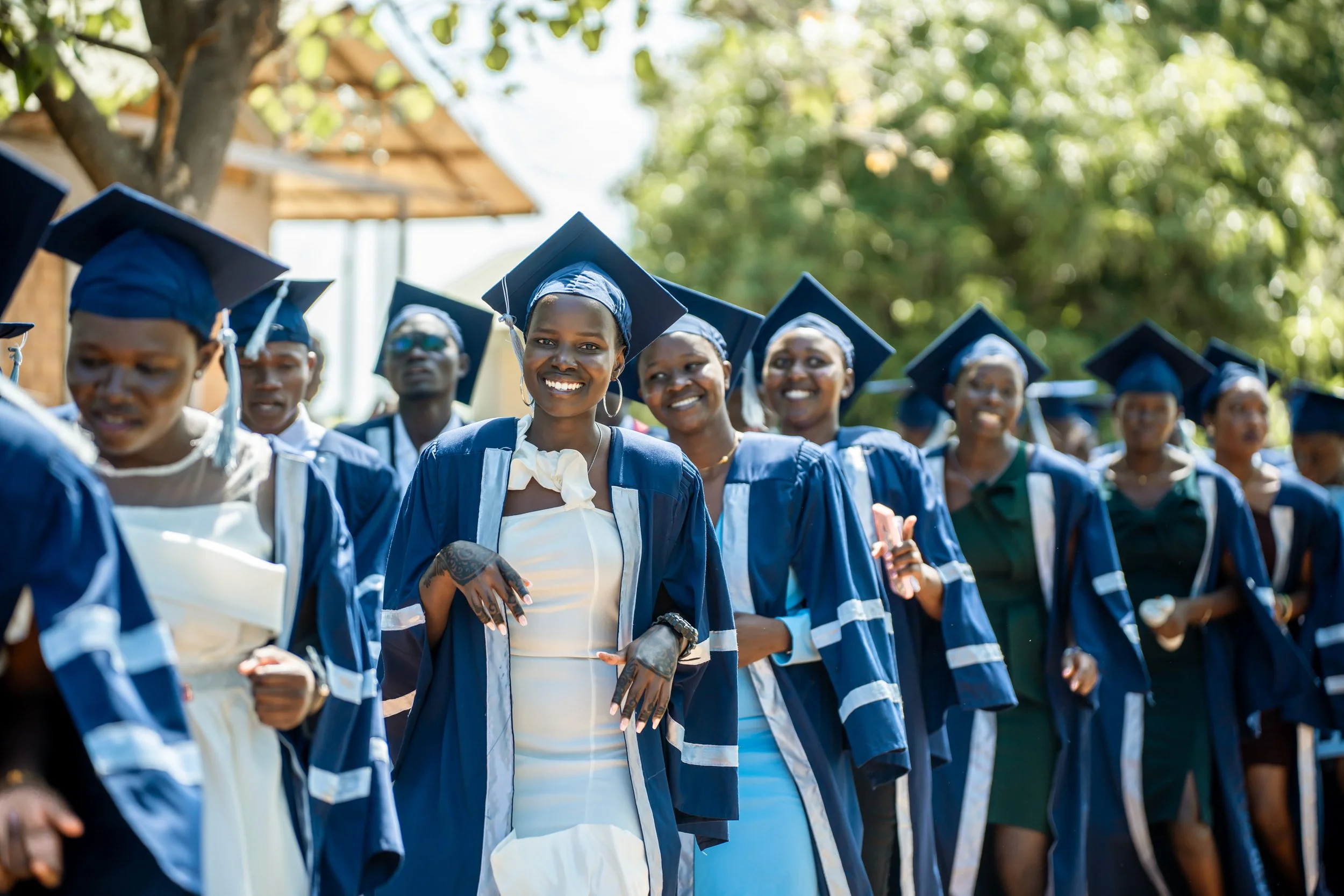 Group of women in graduation gowns and caps smiling during an outdoor ceremony.