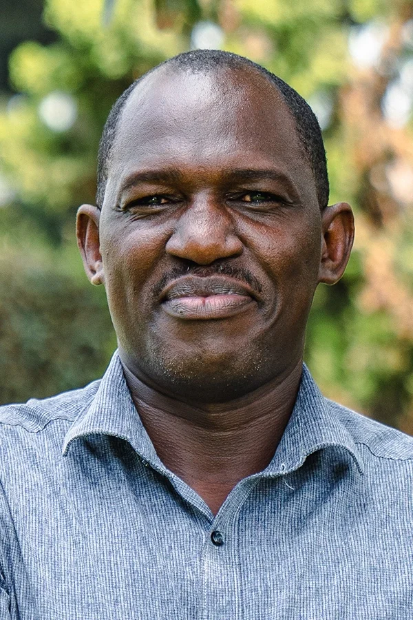 Portrait of a man outdoors, wearing a gray collared shirt, with a blurred natural background.