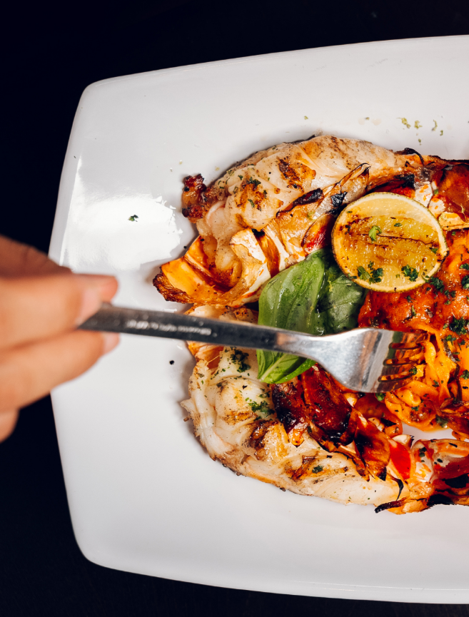 Grilled chicken breast topped with herbs, served with roasted red peppers, a lemon wedge, and fresh basil on a white plate.