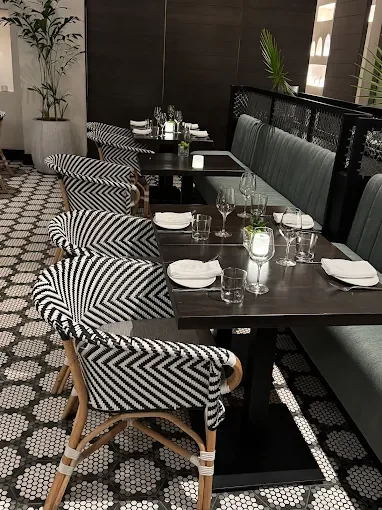 Dining area with black tables, patterned chairs, and a black cushioned bench, set with white plates, glasses, and silverware.