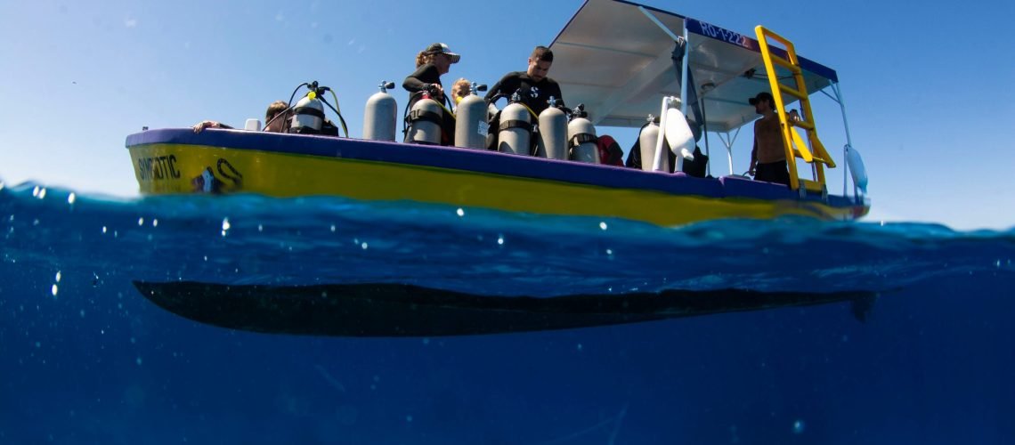 A group of divers on a yellow boat preparing to dive, with scuba tanks and diving gear, on a clear sunny day in the ocean.