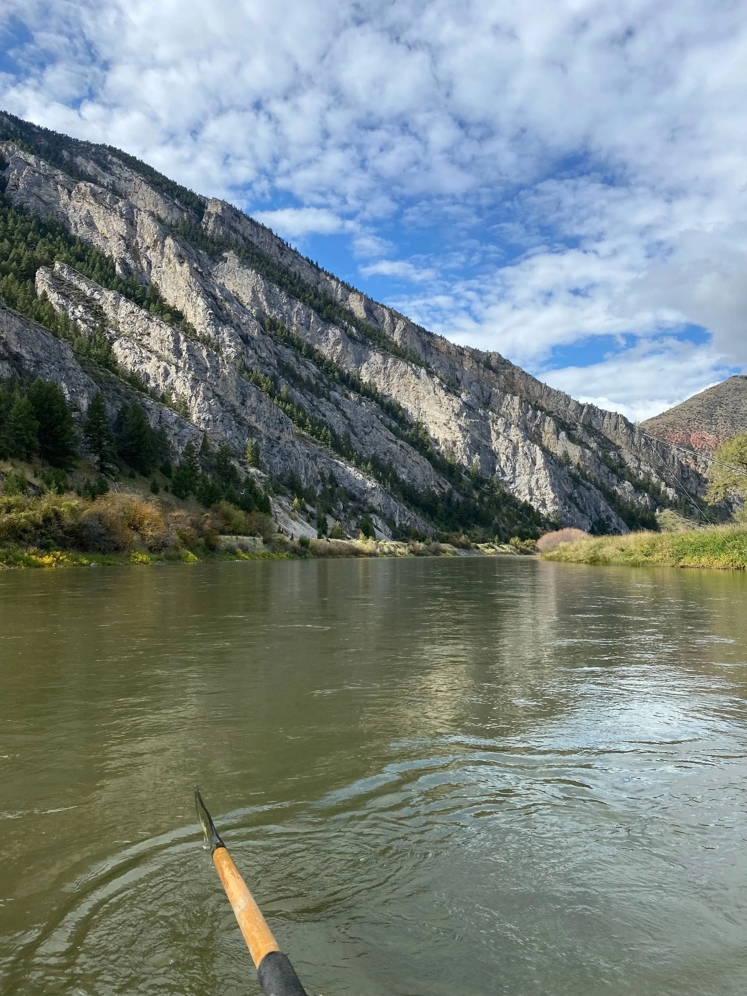 River flowing through a valley with steep, rocky mountains on either side under a partly cloudy sky.