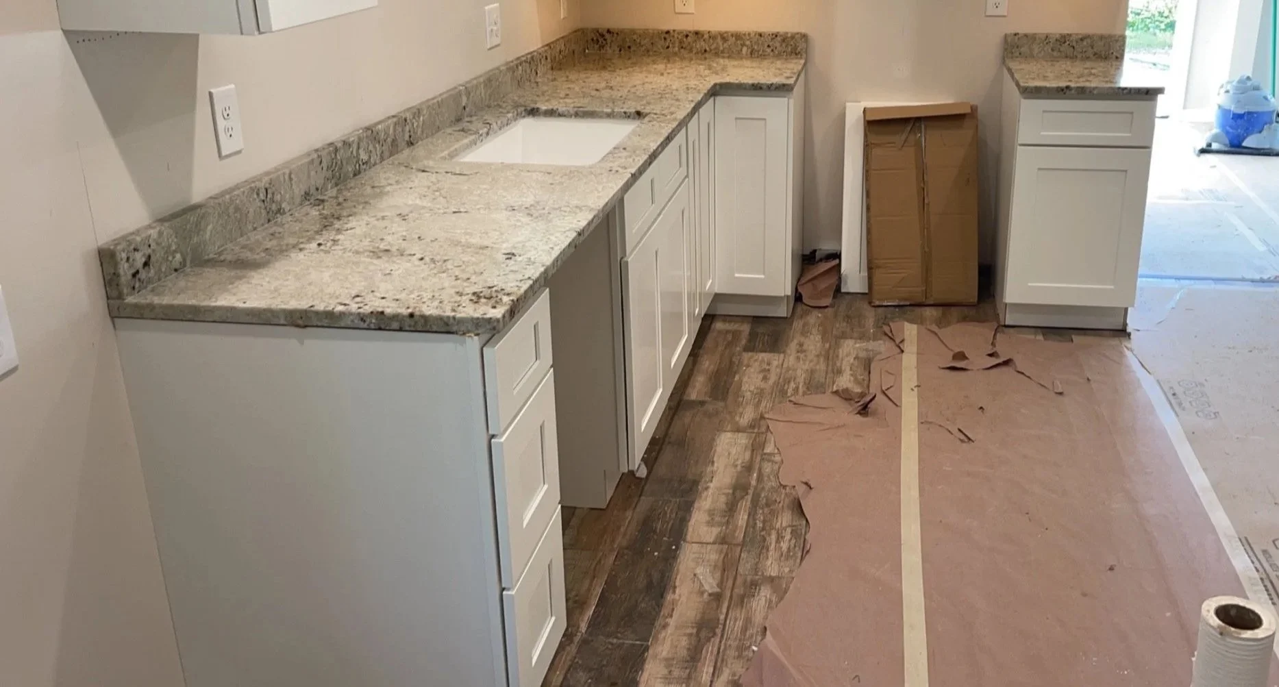 Kitchen with granite countertops, white cabinets, partially installed flooring, and construction materials and tools.