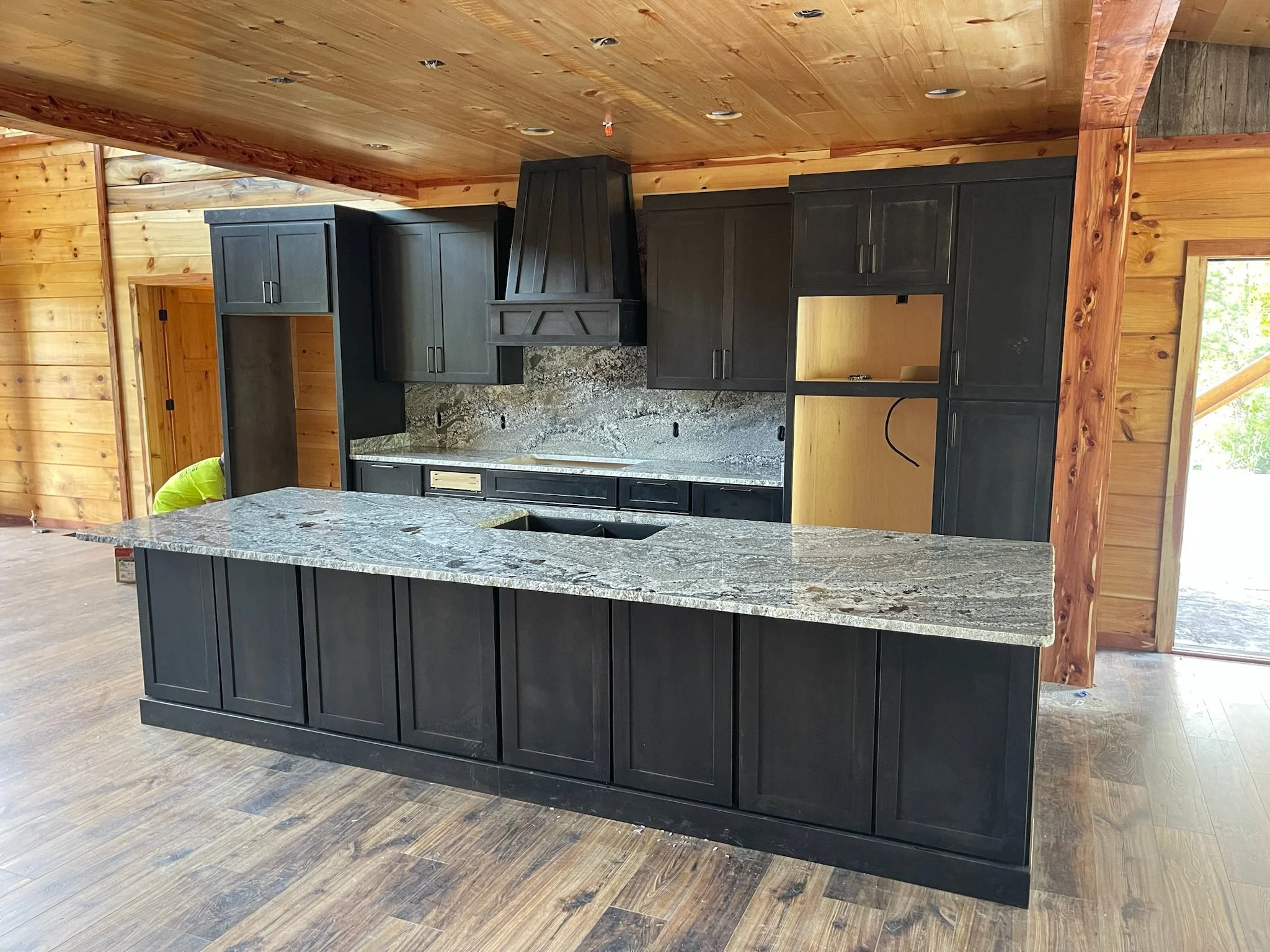 Kitchen with dark cabinets, granite countertops, and wood-paneled walls and ceiling, under construction.