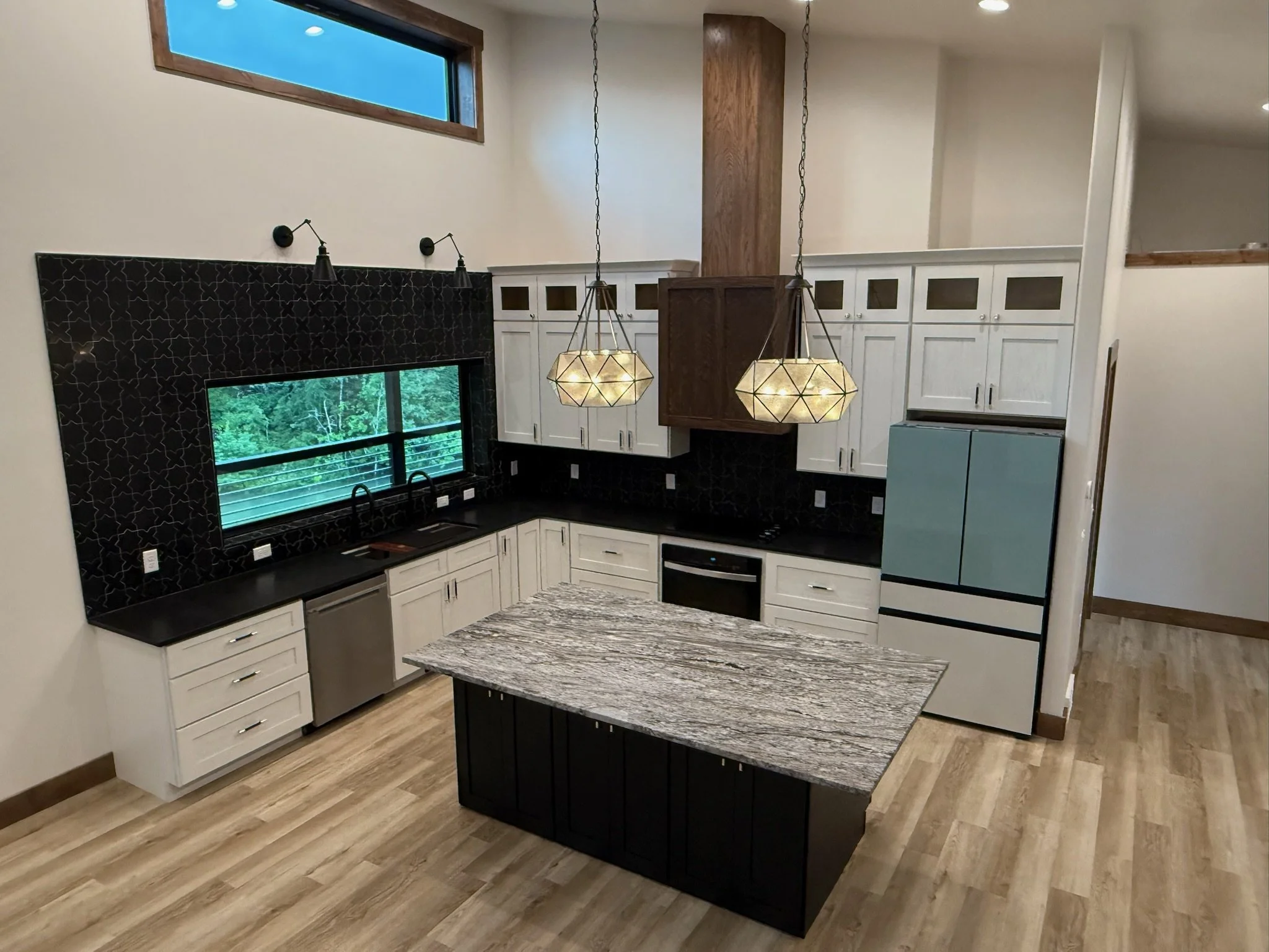 Modern kitchen with white cabinets, black countertops, a granite kitchen island, black tiled backsplash, and two geometric pendant lights hanging over the island.
