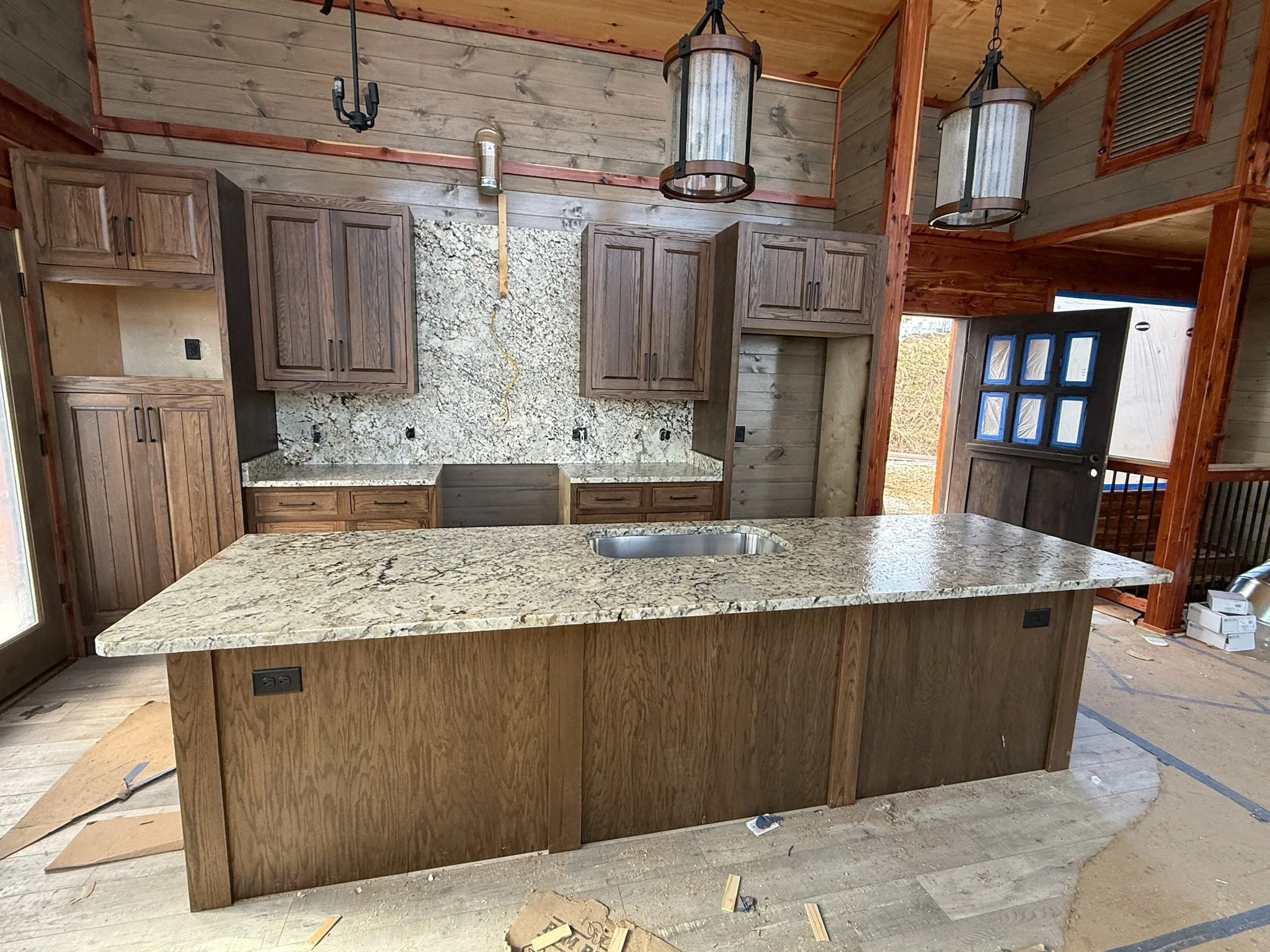 Kitchen with wooden cabinets, granite countertops, island, and partially finished walls and ceiling in a rustic style.