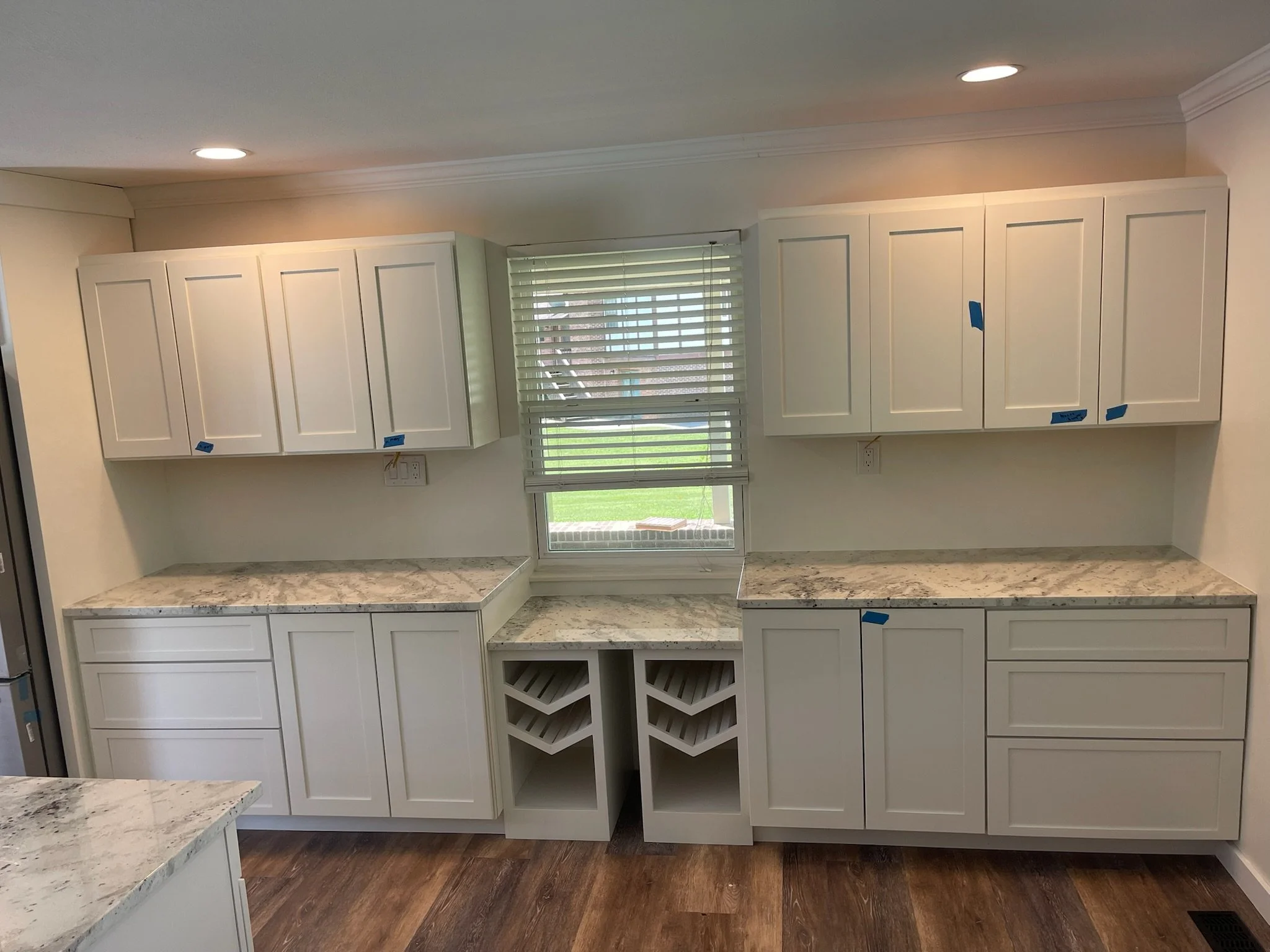 Kitchen with white cabinets, marble countertops, a window with blinds, and wood flooring.