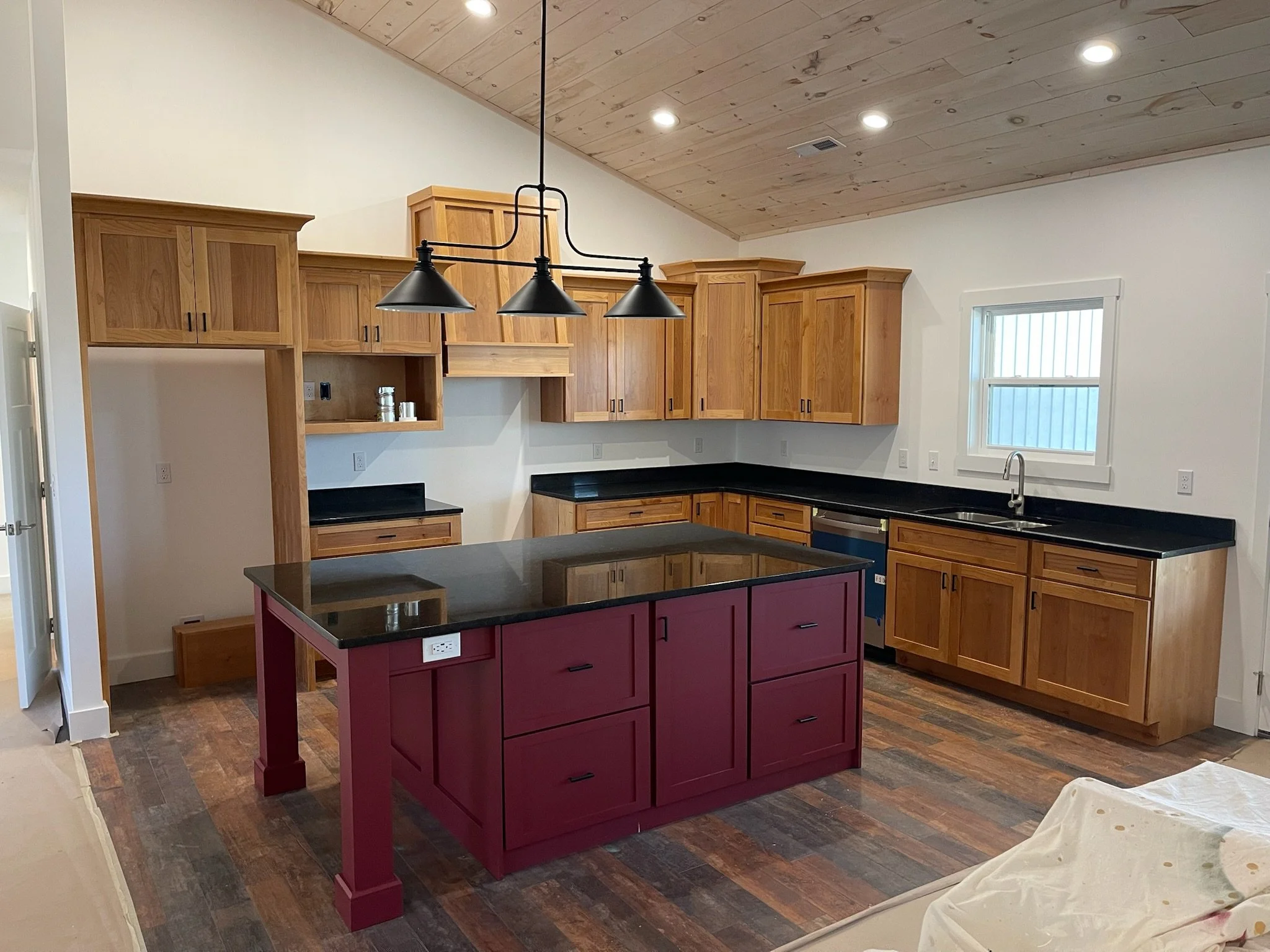 Kitchen with wooden cabinets, black countertops, a red kitchen island, and a window above the sink.