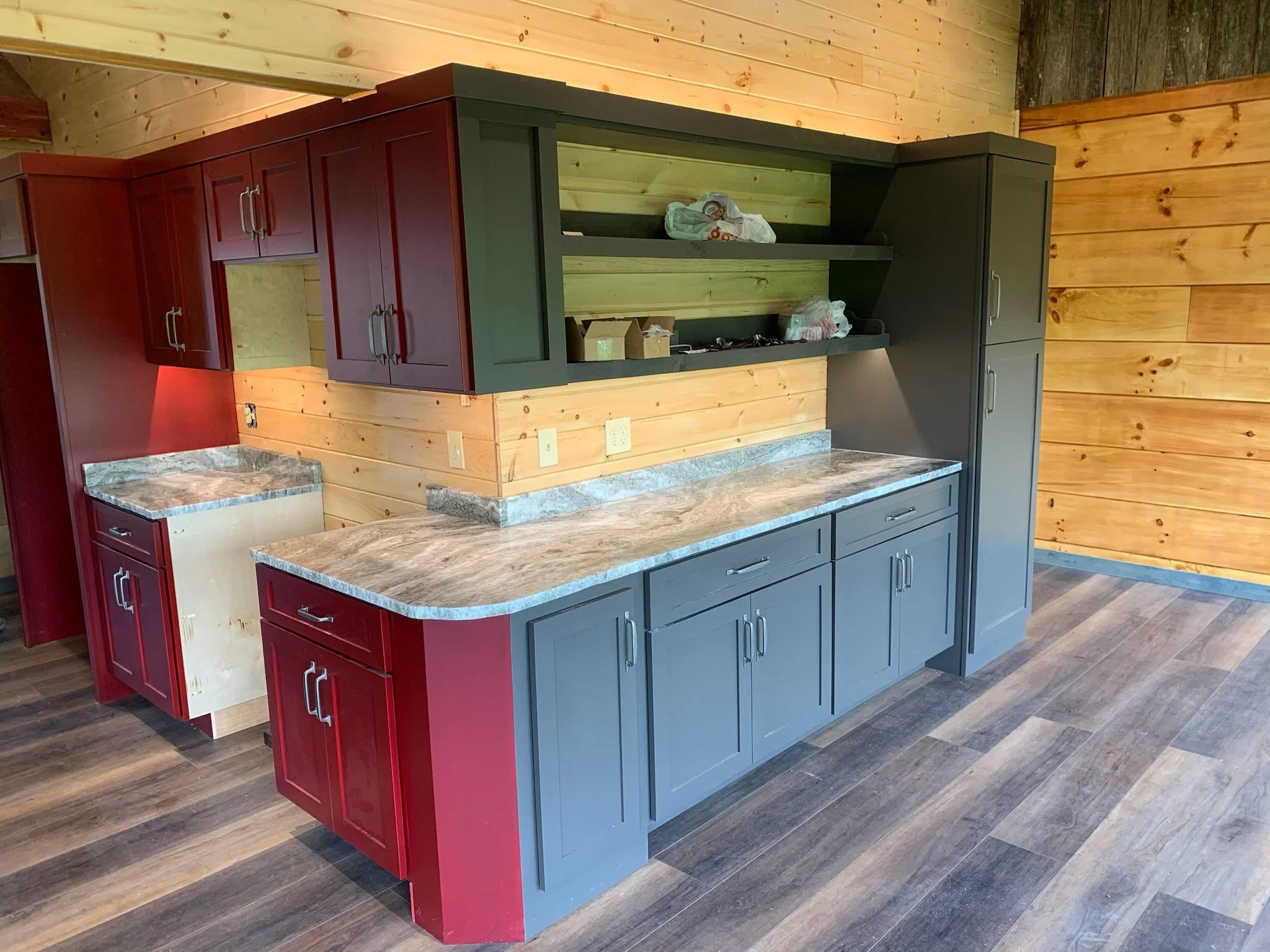 Interior of a kitchen under construction with red and black cabinets, a marble countertop, and wooden wall paneling.