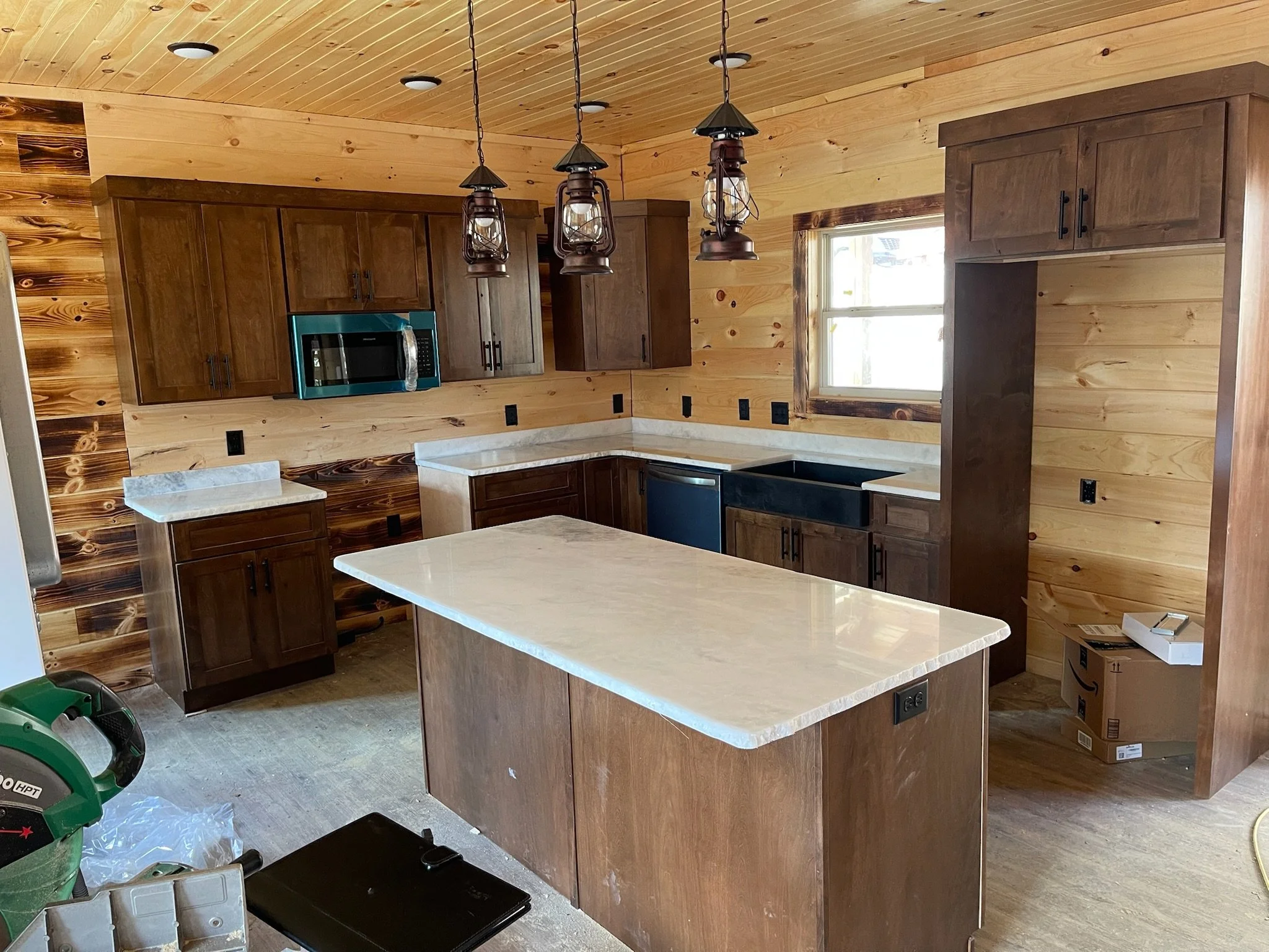 Kitchen with wooden cabinets, a central island with a light-colored countertop, a black sink, a window, and rustic hanging light fixtures.