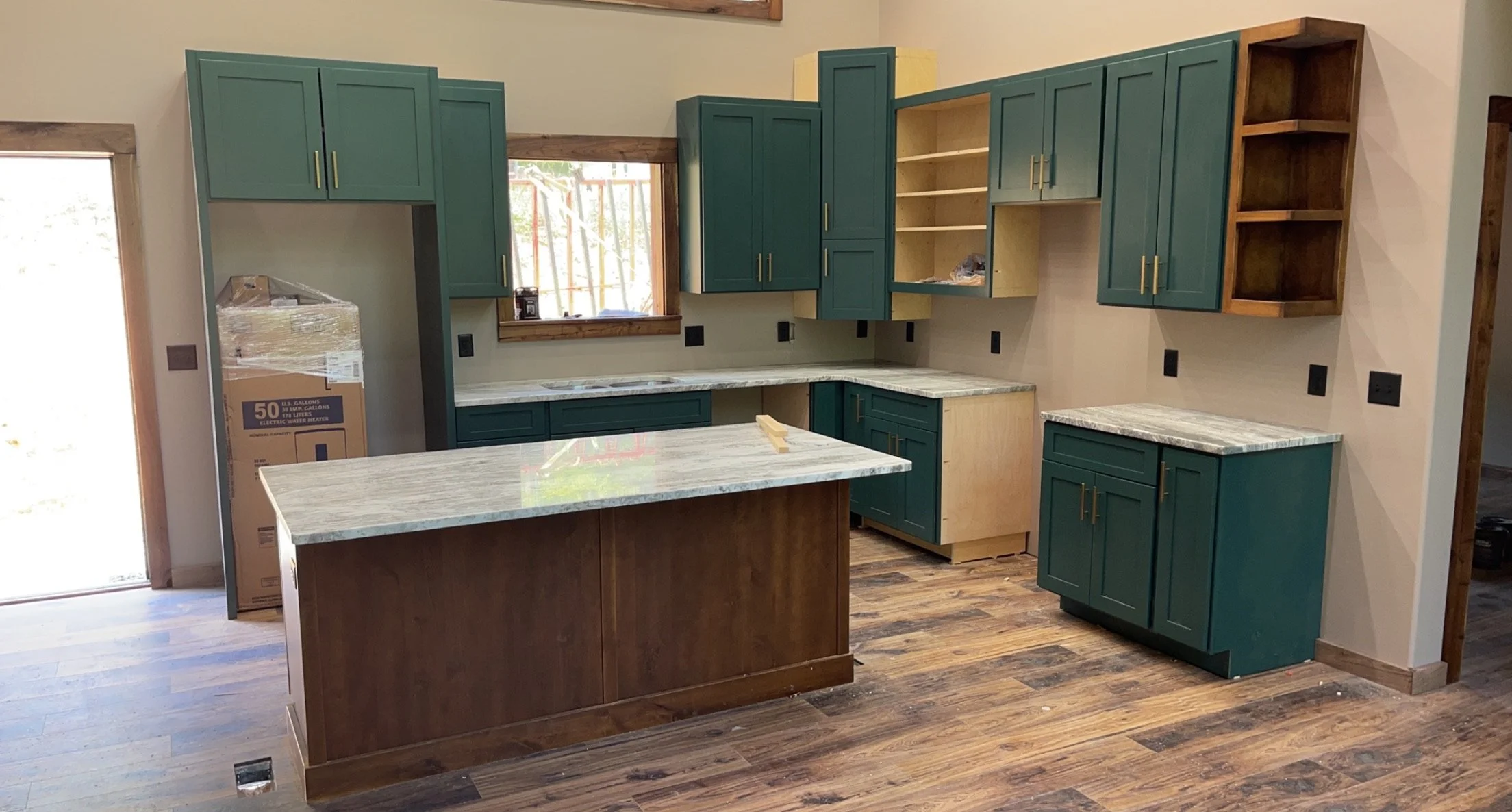 Kitchen under construction with green and wood cabinets, granite countertops, hardwood floors, and a small island with a matching countertop.