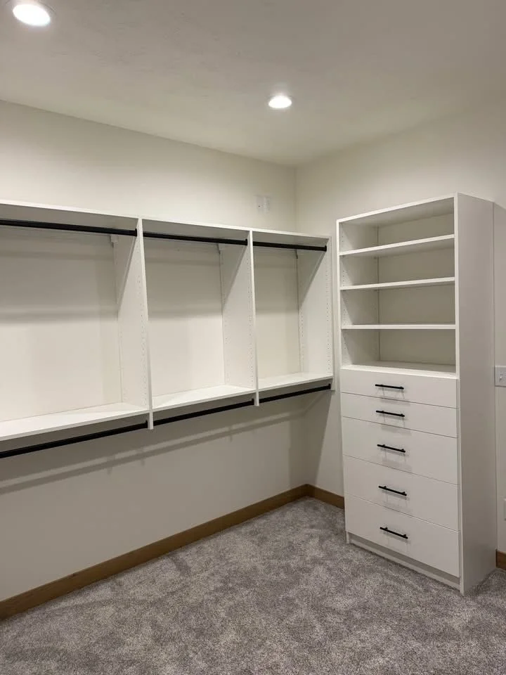 Empty walk-in closet with built-in white shelving and drawers, carpeted floor, and recessed ceiling lights.