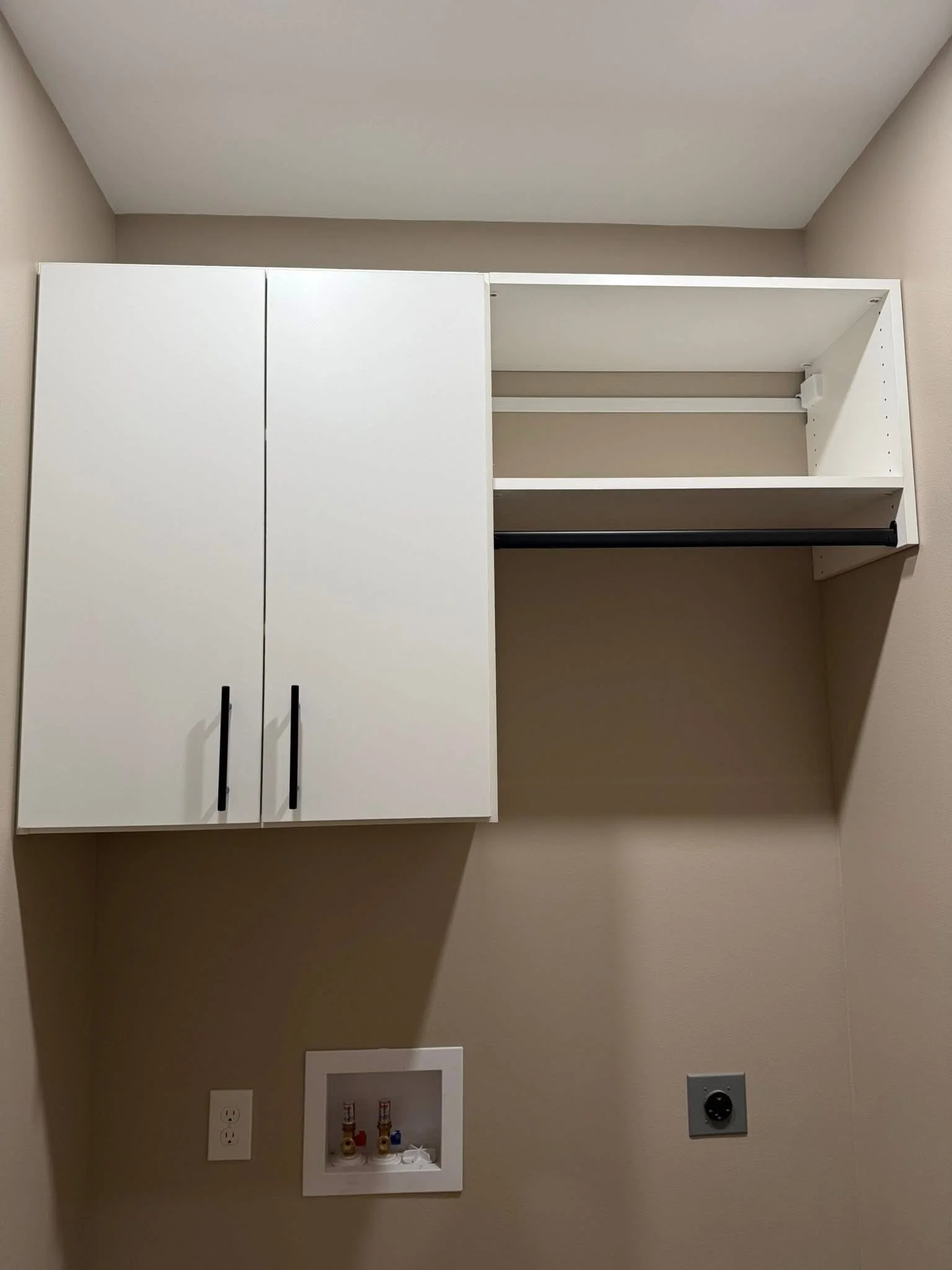 Empty laundry room with white cabinets, beige walls, and plumbing outlets.