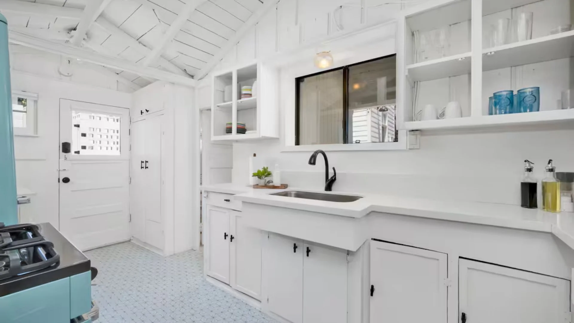 Bright white kitchen with open shelving, black faucet, and a window above the sink.