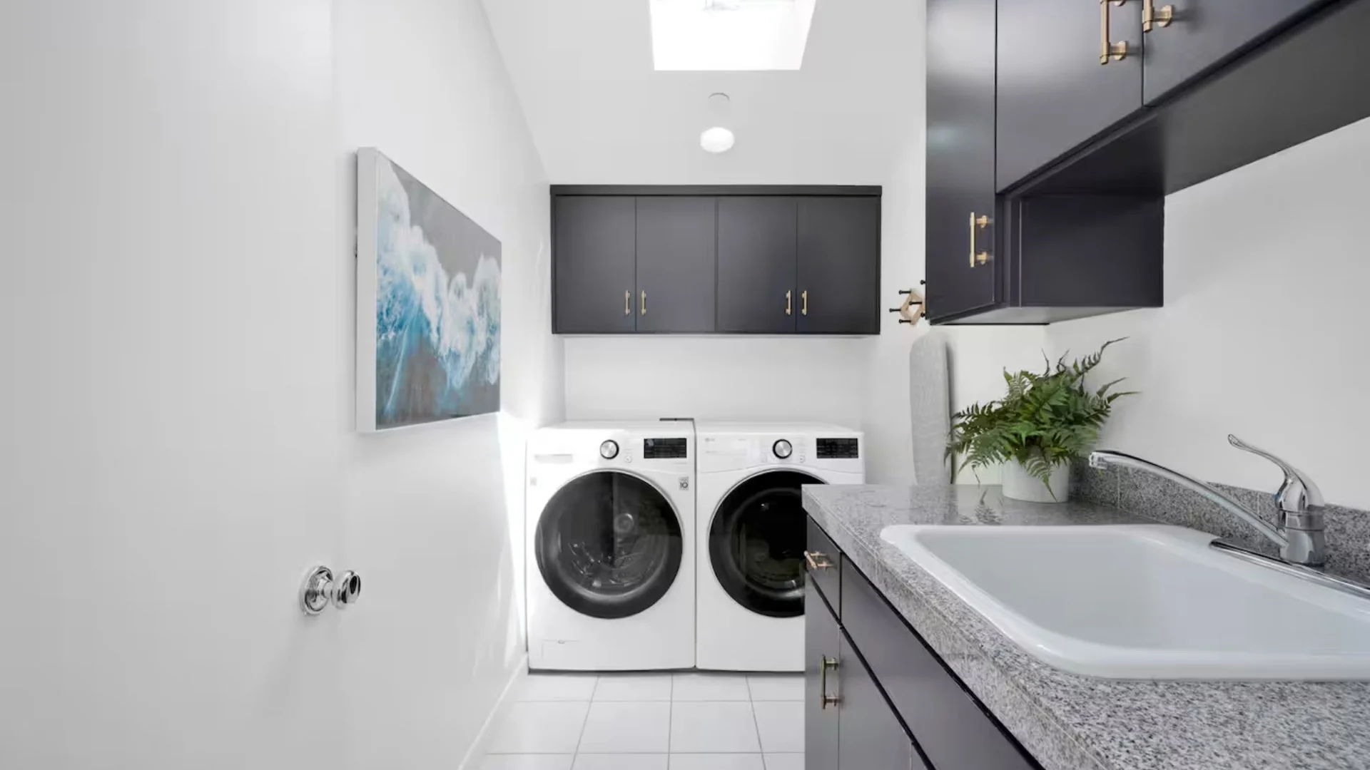 Laundry room with white washer and dryer, dark cabinets, gray countertop with a sink, and a plant.