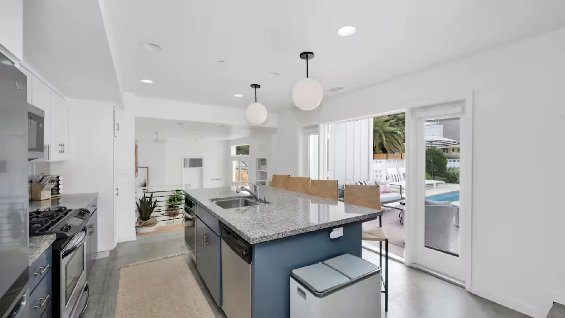 Modern kitchen with granite countertop island, stainless steel appliances, and patio door leading outside to a pool and seating area.