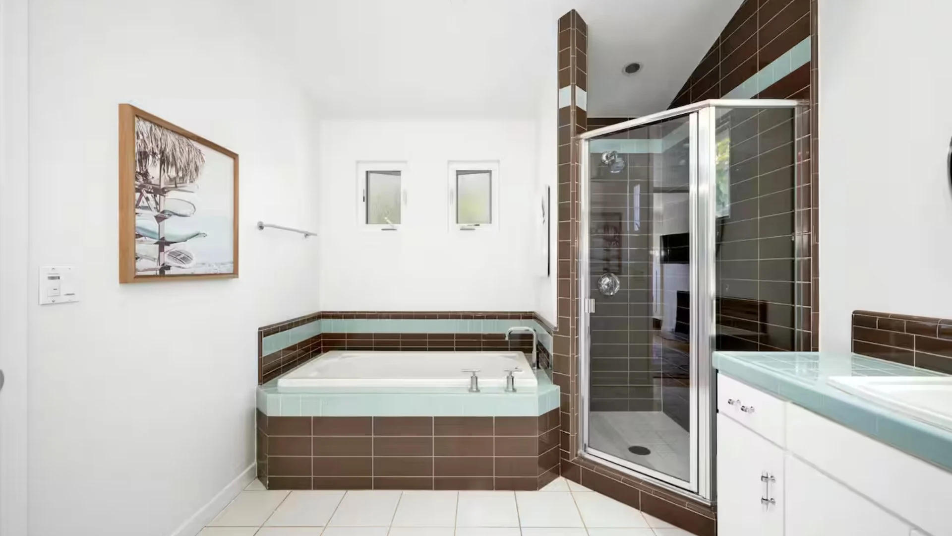 Modern bathroom with a corner bathtub, glass shower enclosure, white cabinets, and white walls with a framed picture.