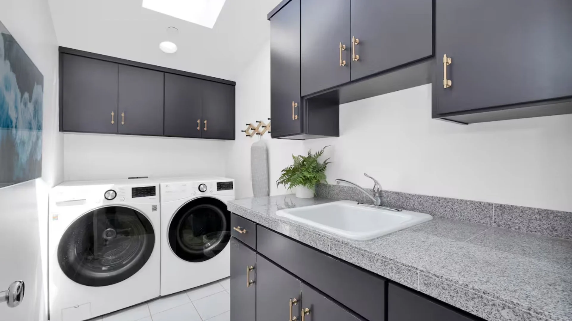 Laundry room with white front-loading washer and dryer, dark blue cabinets, granite countertop, white sink, and a plant on the counter.