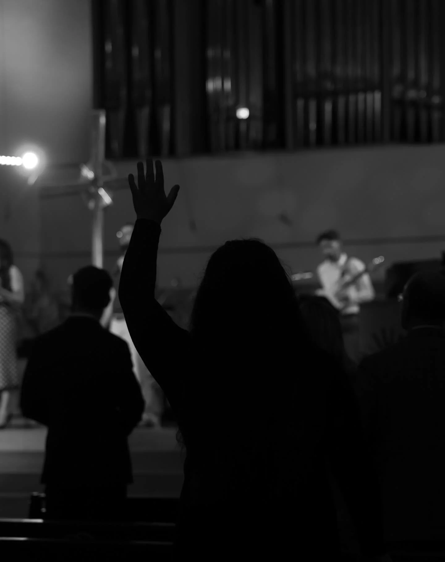 Black and white photo of a person raising their hand in a room with a band performing on stage in the background.